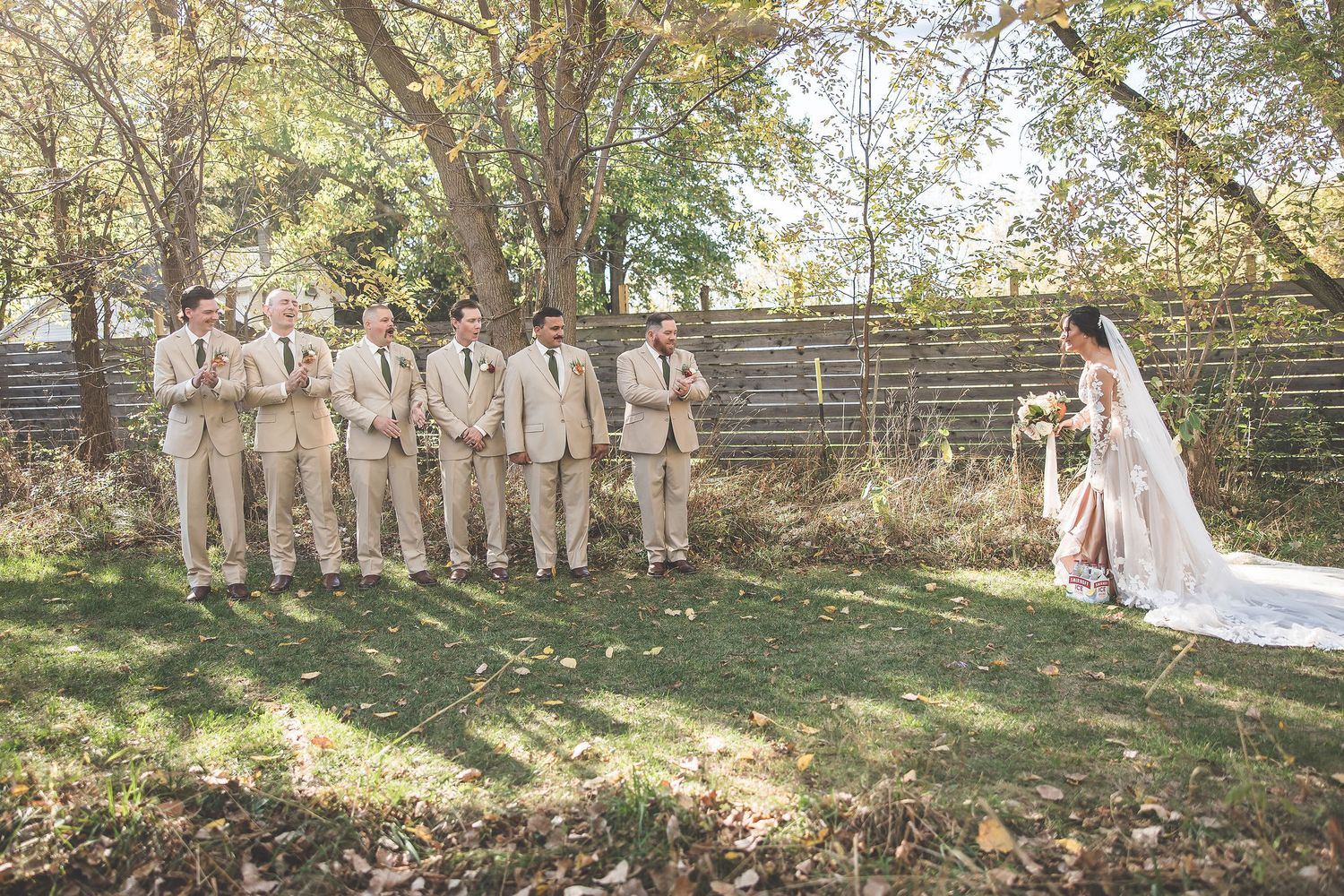 Wedding party in tan suits and light dresses standing together in a scenic outdoor garden setting.