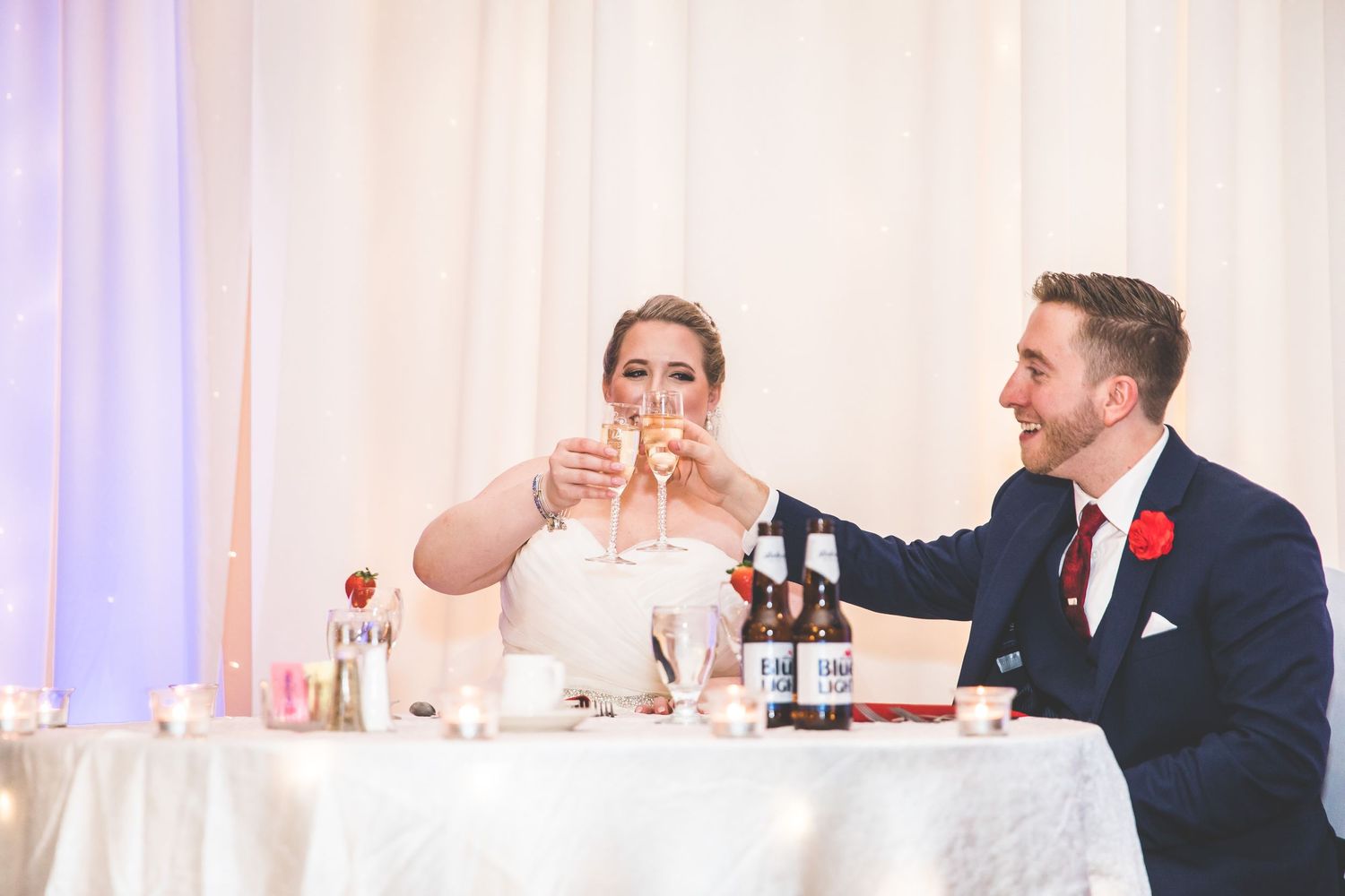 Couple toasts with champagne glasses at their wedding reception head table.