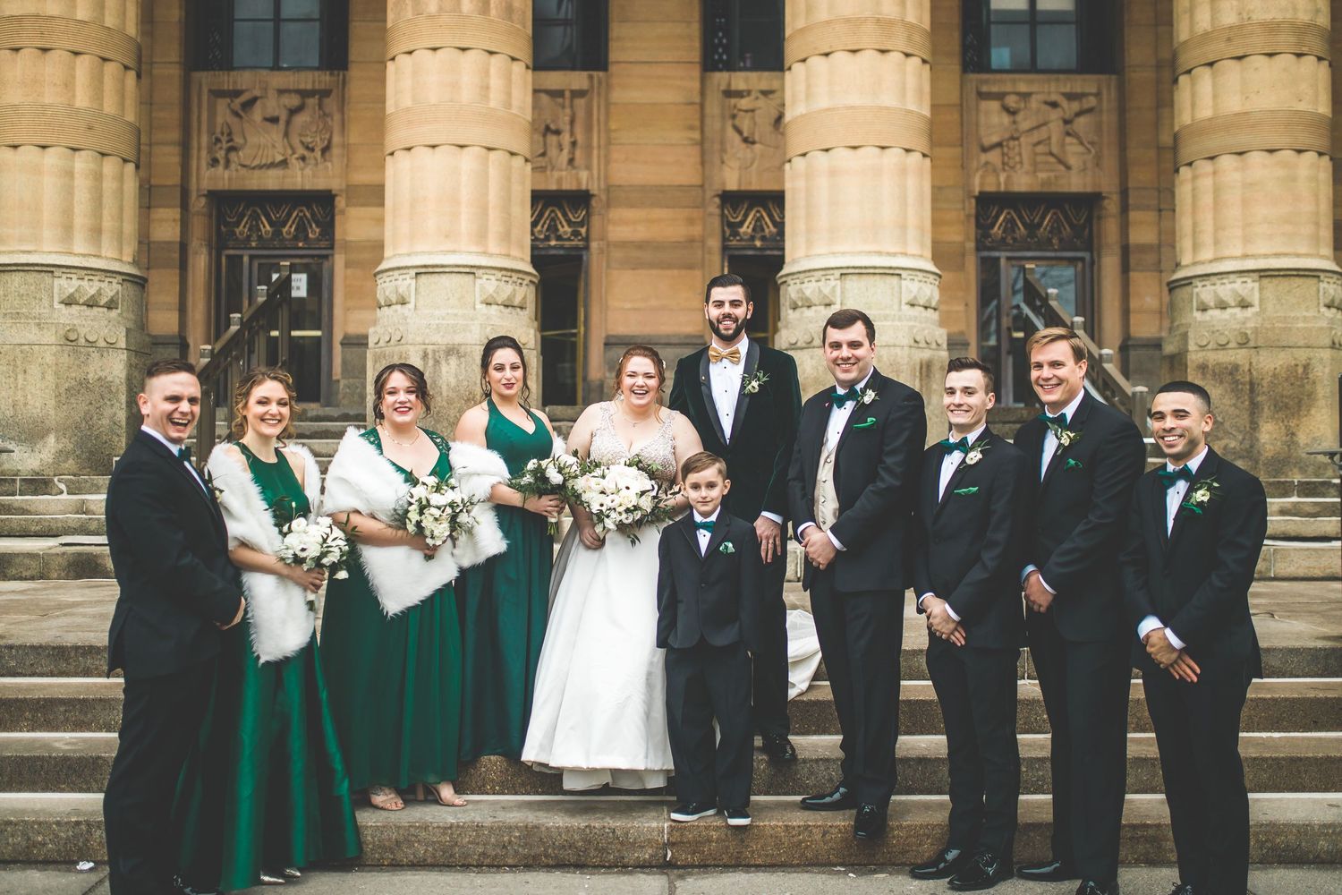 Wedding party in emerald green and black formal attire posed on stone steps.