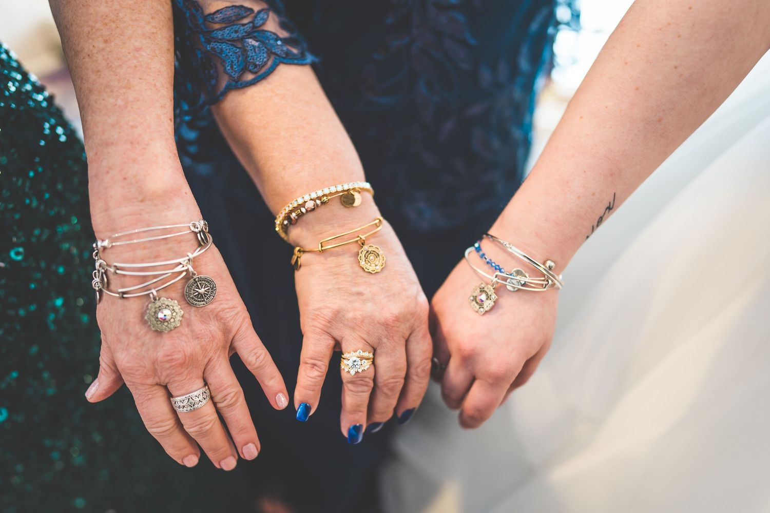 Multiple hands displaying wedding rings and bracelets against a dark blue background.