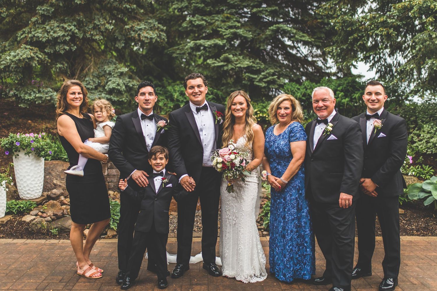 Wedding party and guests celebrating outdoors among trees and greenery.