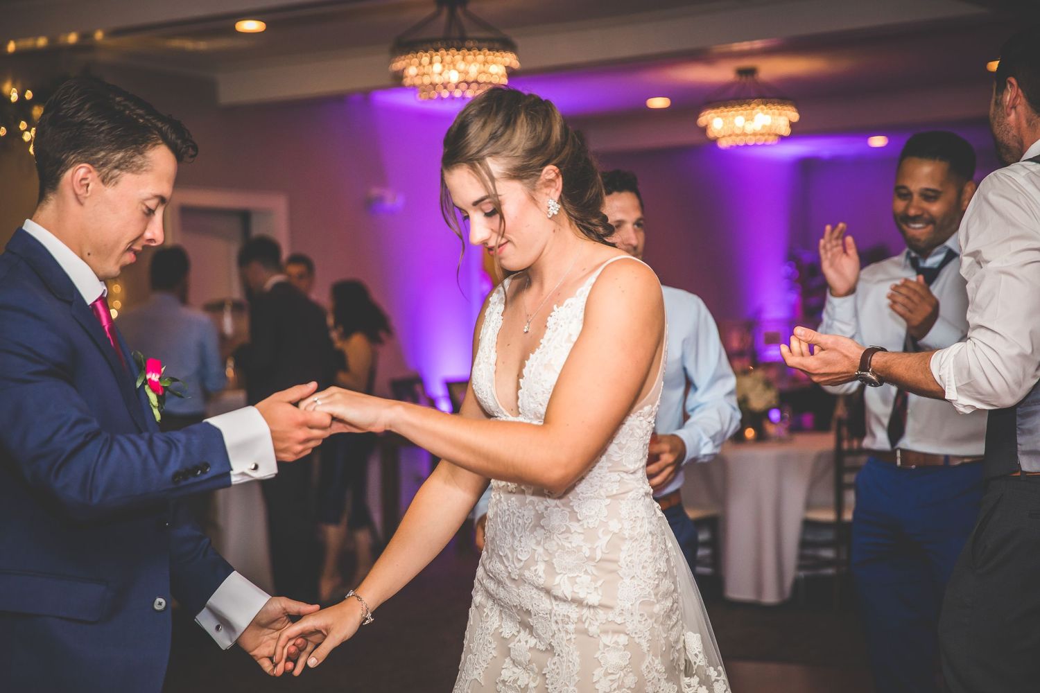 Wedding party dancing and celebrating during reception with purple lighting effects.
