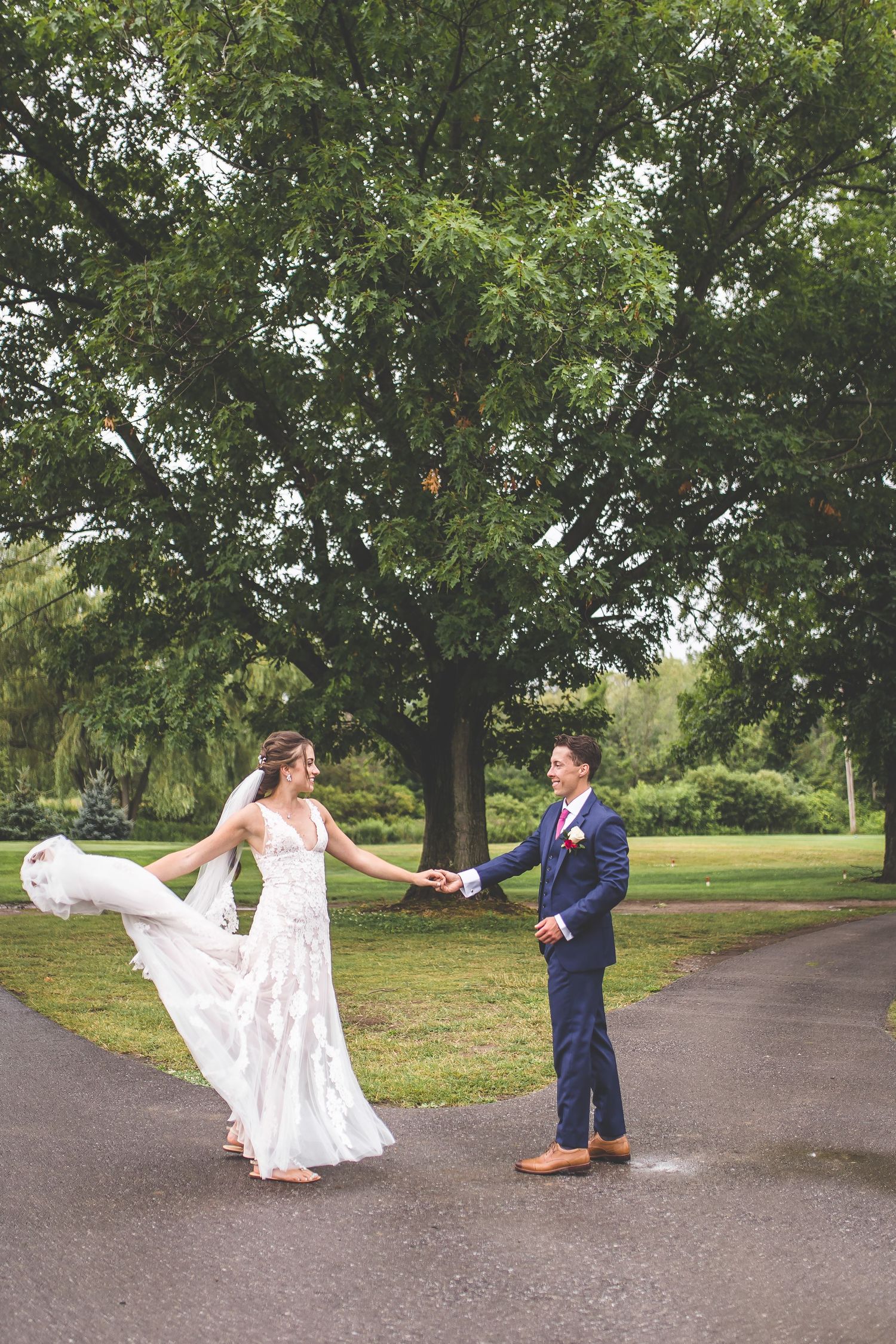 Wedding couple dances playfully on a tree-lined path during their outdoor photo session.