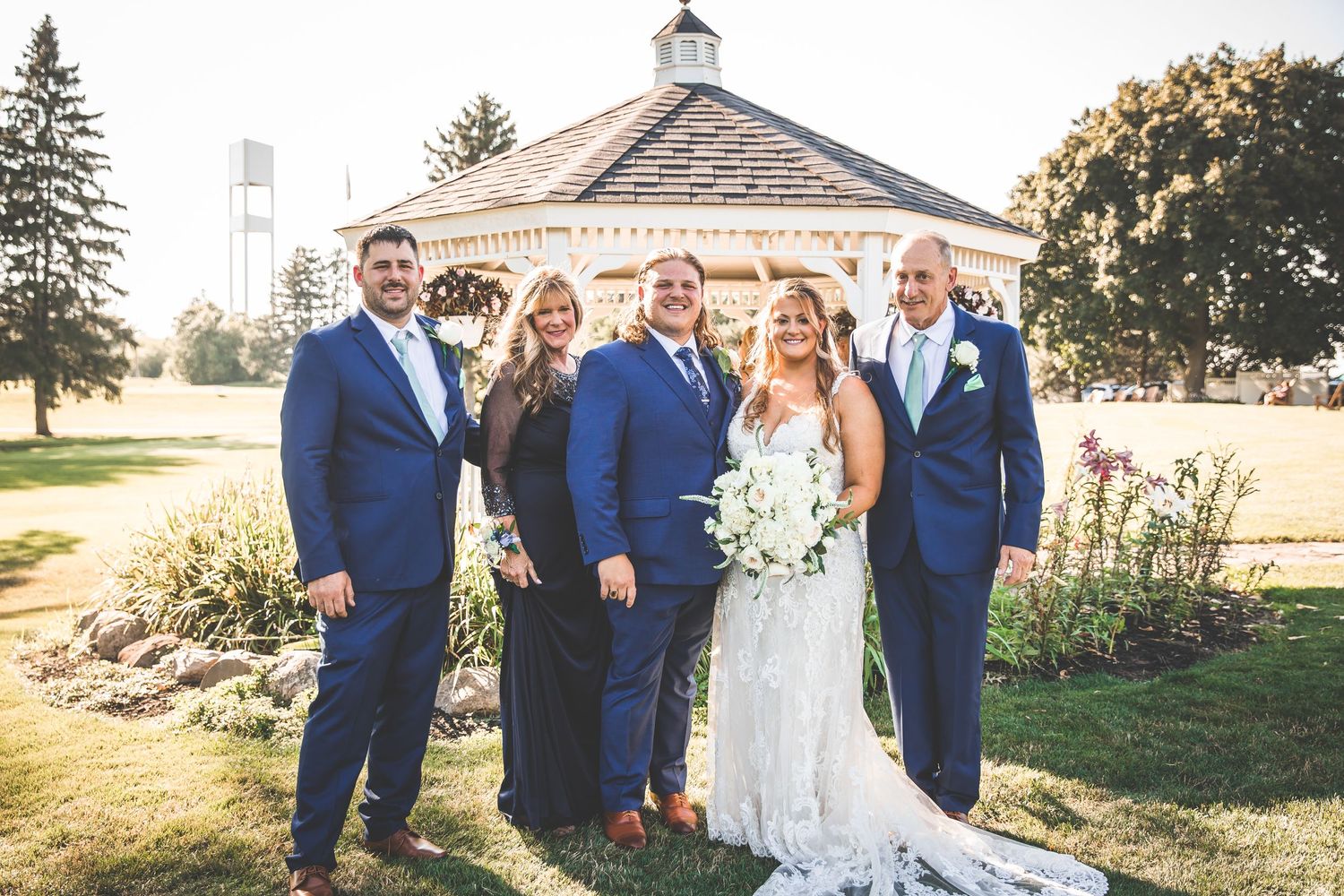 Wedding party poses outside chapel with white steeple in golden afternoon light.
