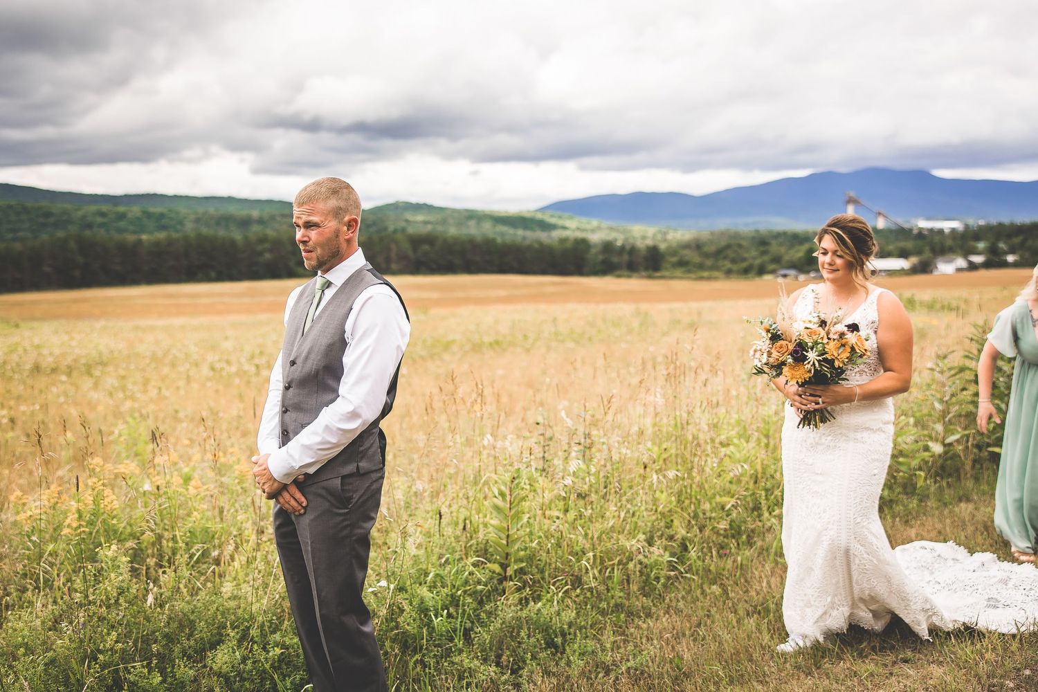Wedding couple posing in a scenic mountain field with dramatic cloudy skies.