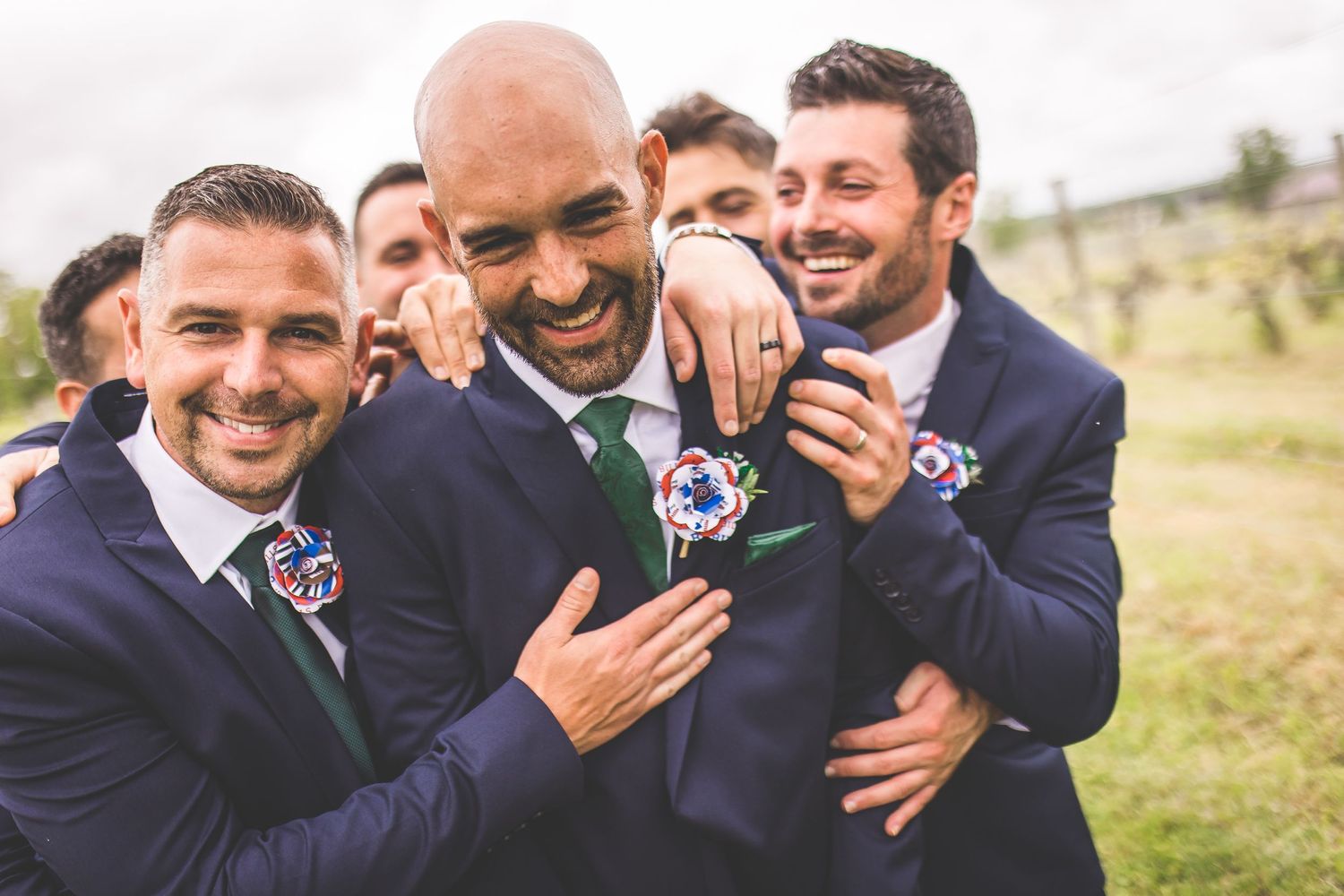 Groomsmen in navy suits share laughs during outdoor wedding photo session.