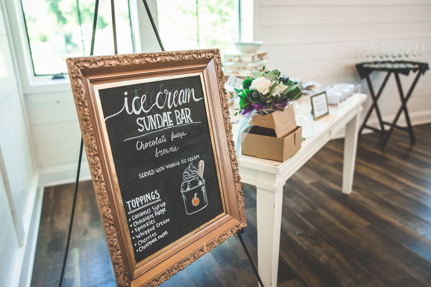 Vintage framed chalkboard sign displaying ice cream sundae bar menu at a wedding reception.