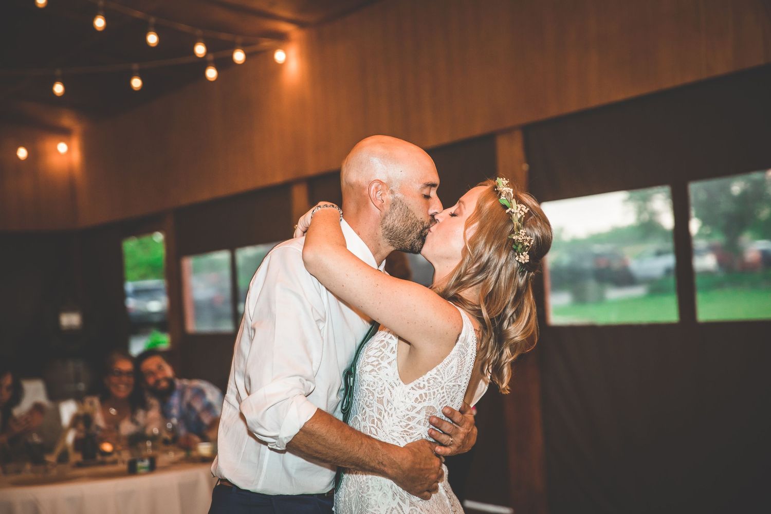 Couples dance together at an indoor wedding reception with warm lighting and string lights overhead.