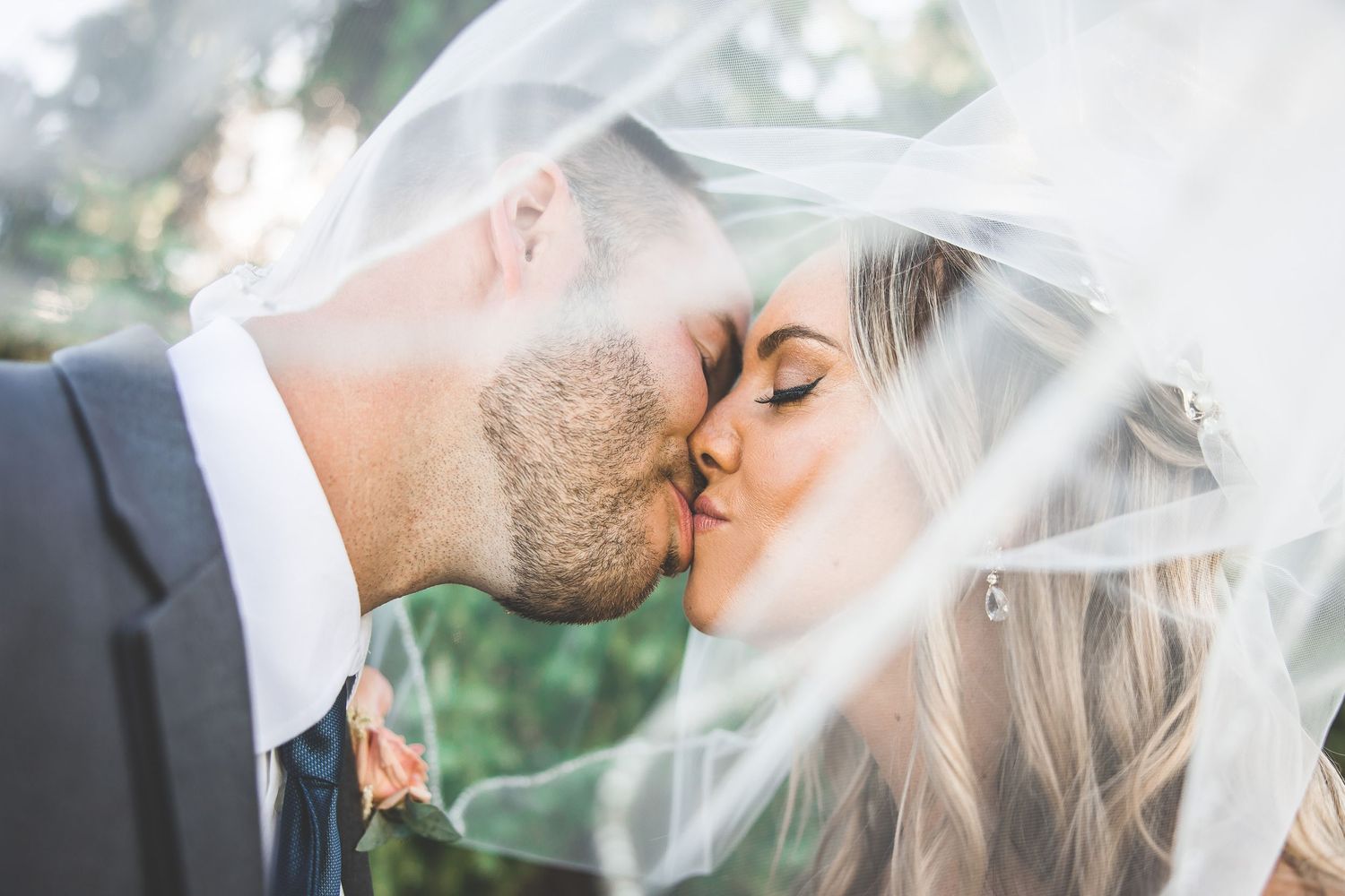 Romantic close-up of newlyweds sharing a kiss under sheer white veil.