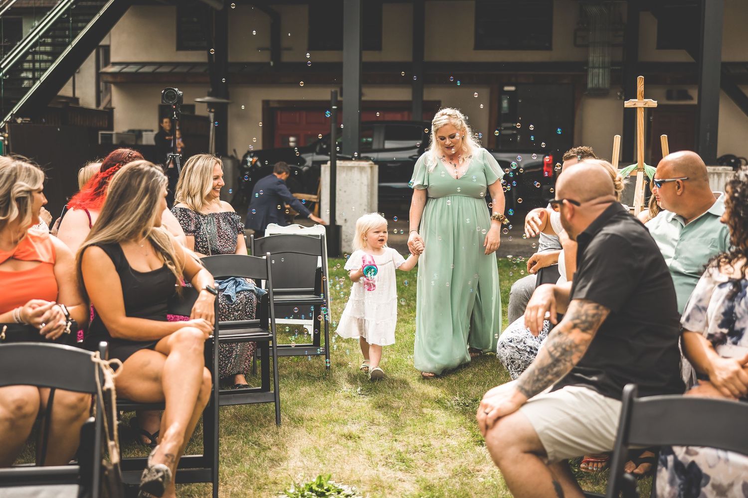 Outdoor wedding ceremony setup with rows of black chairs and guests.