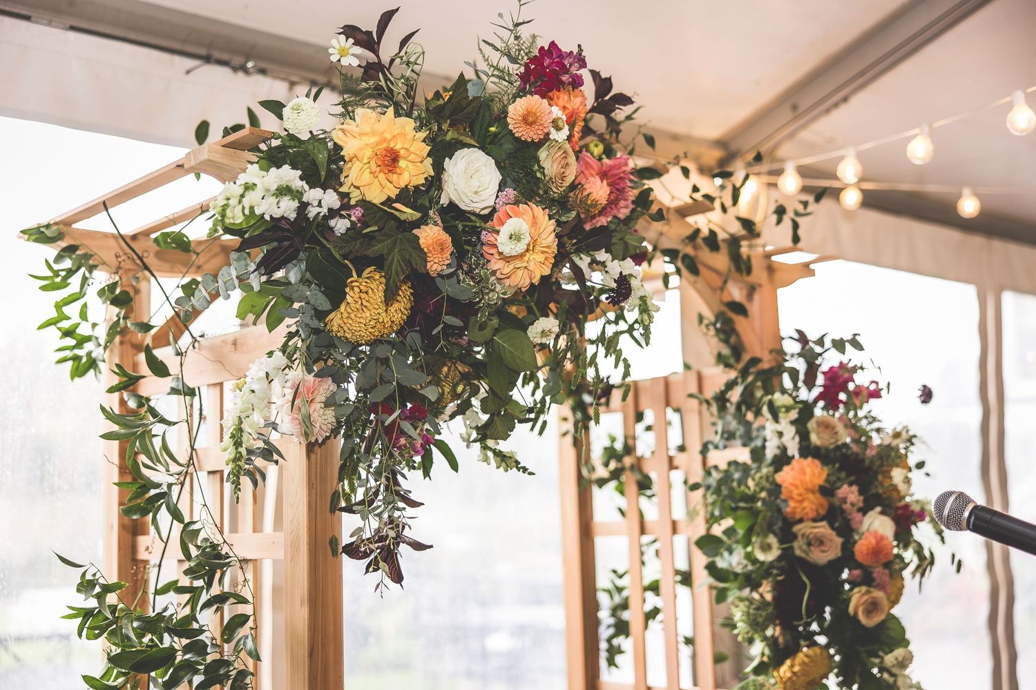 Floral arrangements with orange and pink blooms hang from wooden beams in a wedding venue.