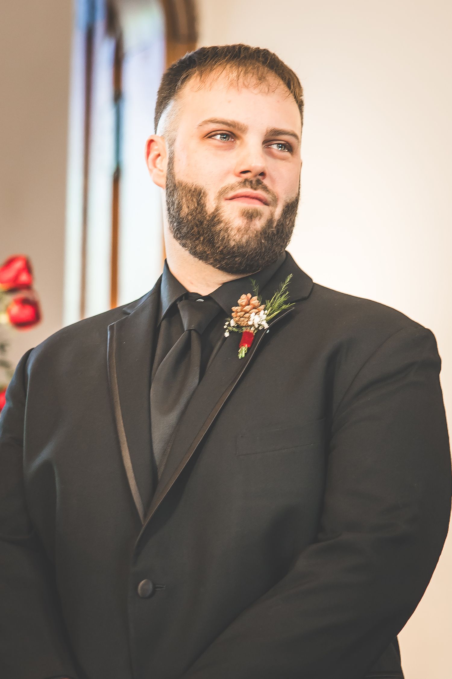 Groom in classic black tuxedo with boutonniere at wedding ceremony.