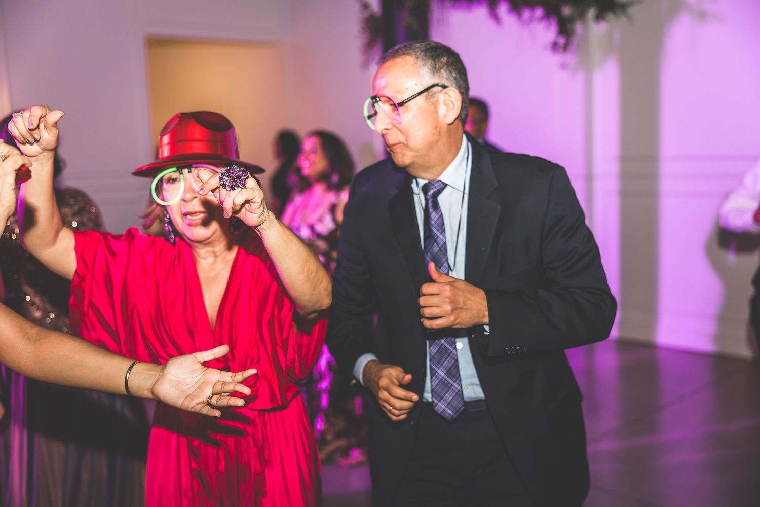 Reception guests dancing and socializing under purple mood lighting at an indoor venue.