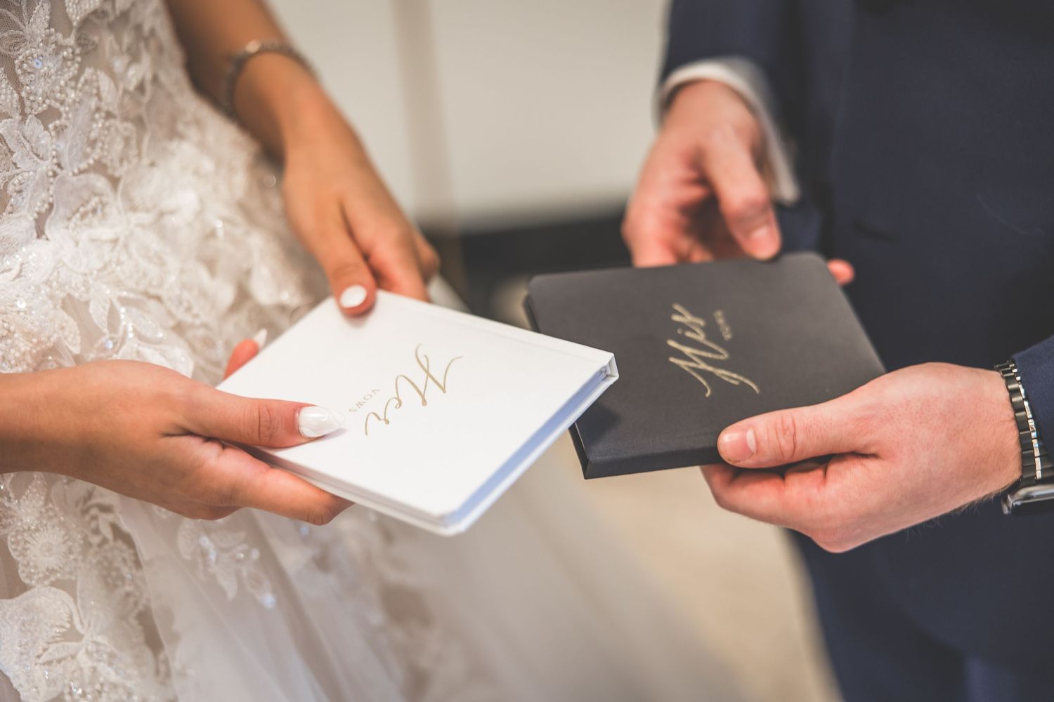 Close-up of bride and groom exchanging vow books during wedding ceremony.