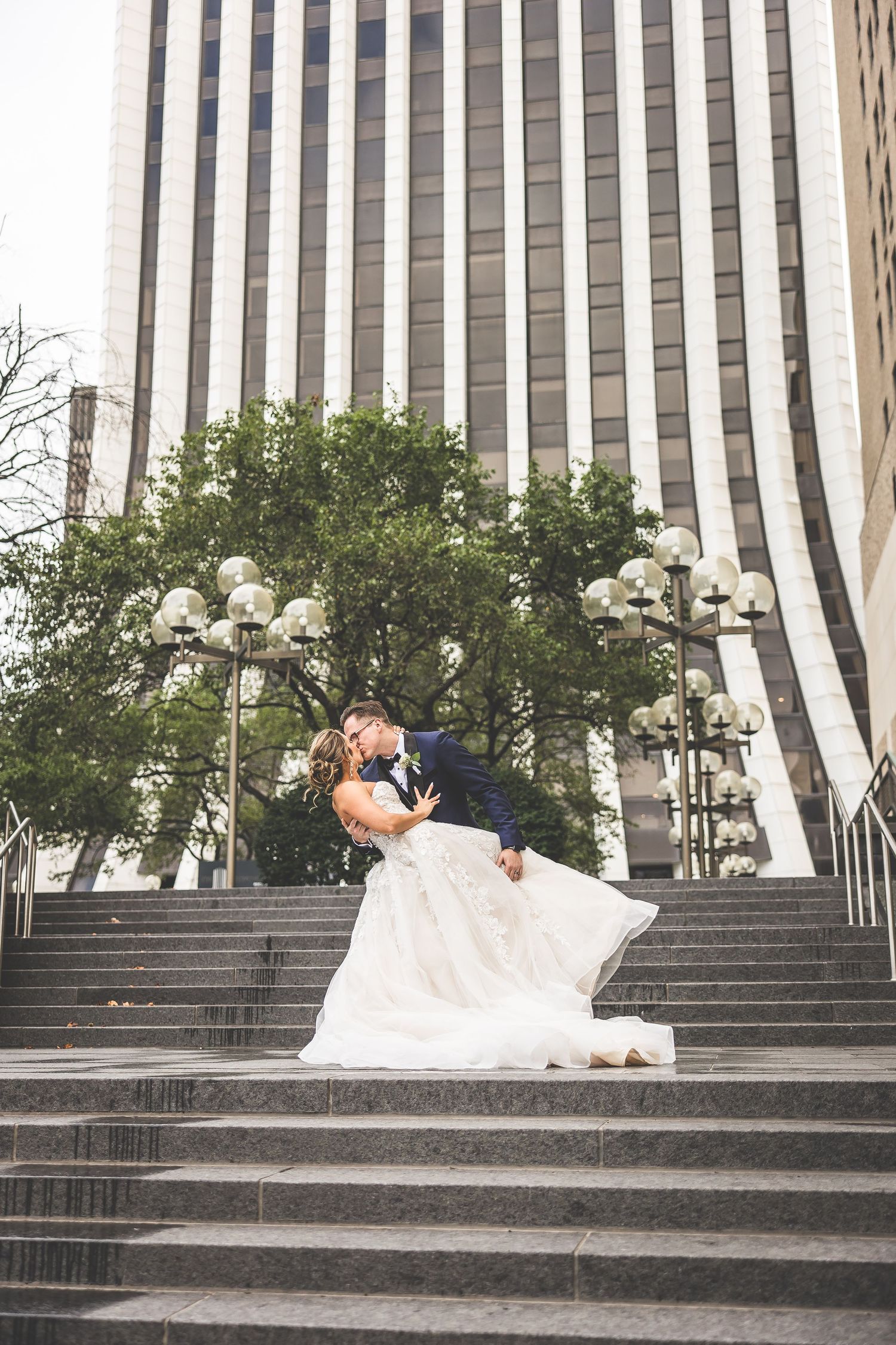 Wedding couple shares a playful moment on wide stone steps with urban architecture in background.
