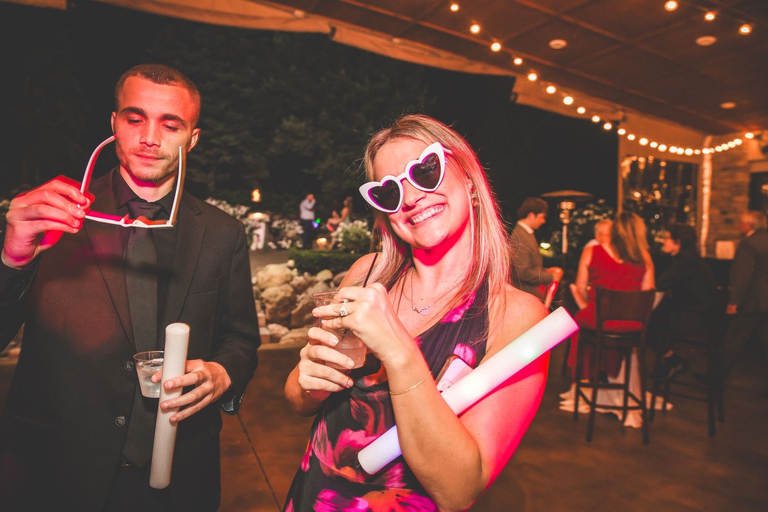 Party guests dance and celebrate under warm string lights at a nighttime wedding reception.