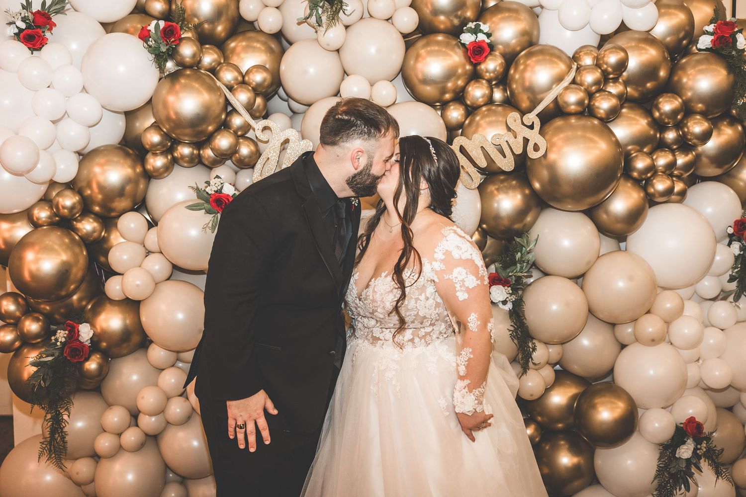 Elegant wedding backdrop featuring a luxurious gold and white balloon arch with twinkling lights.