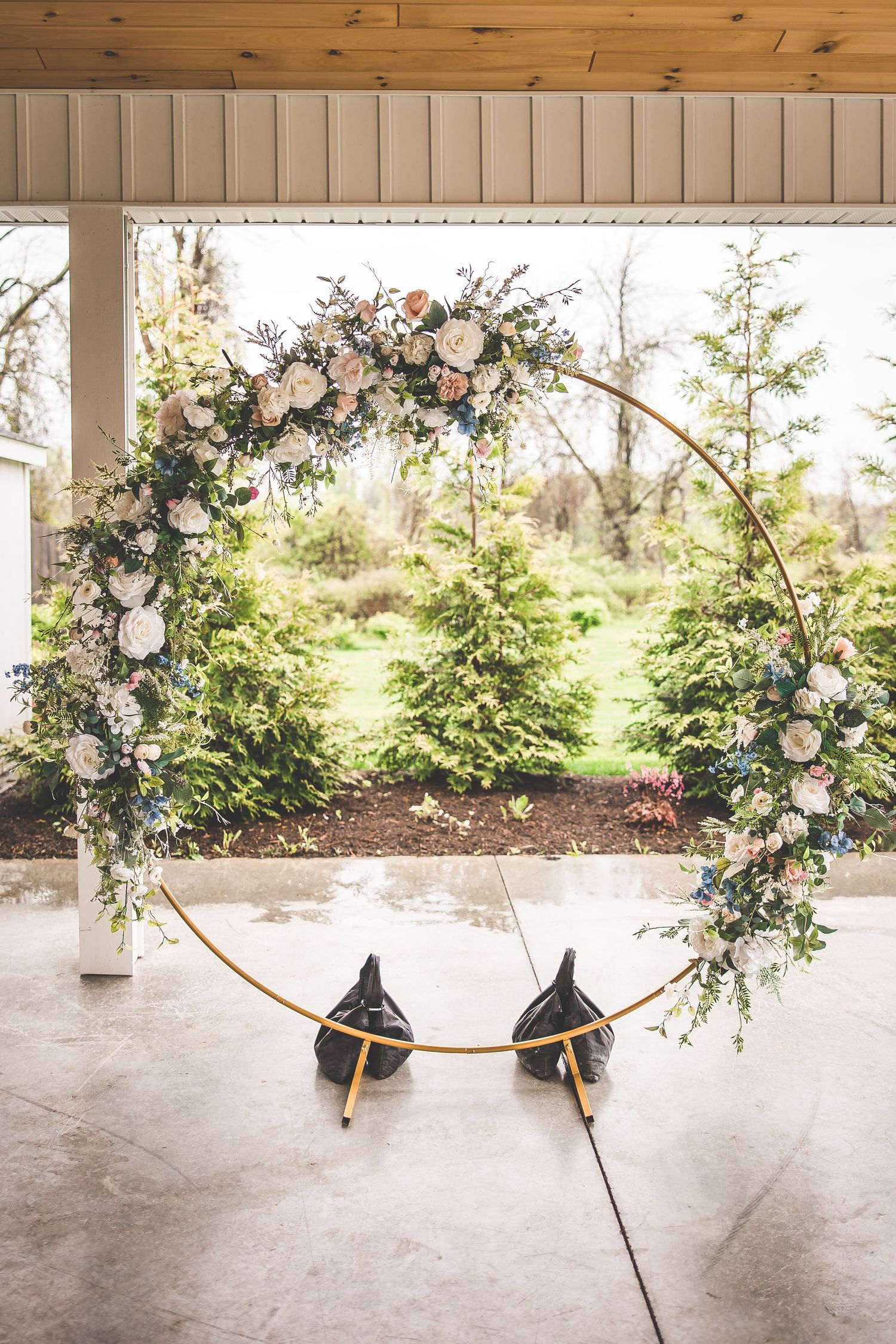 A circular floral wedding arch with pink and white roses against a natural outdoor backdrop.