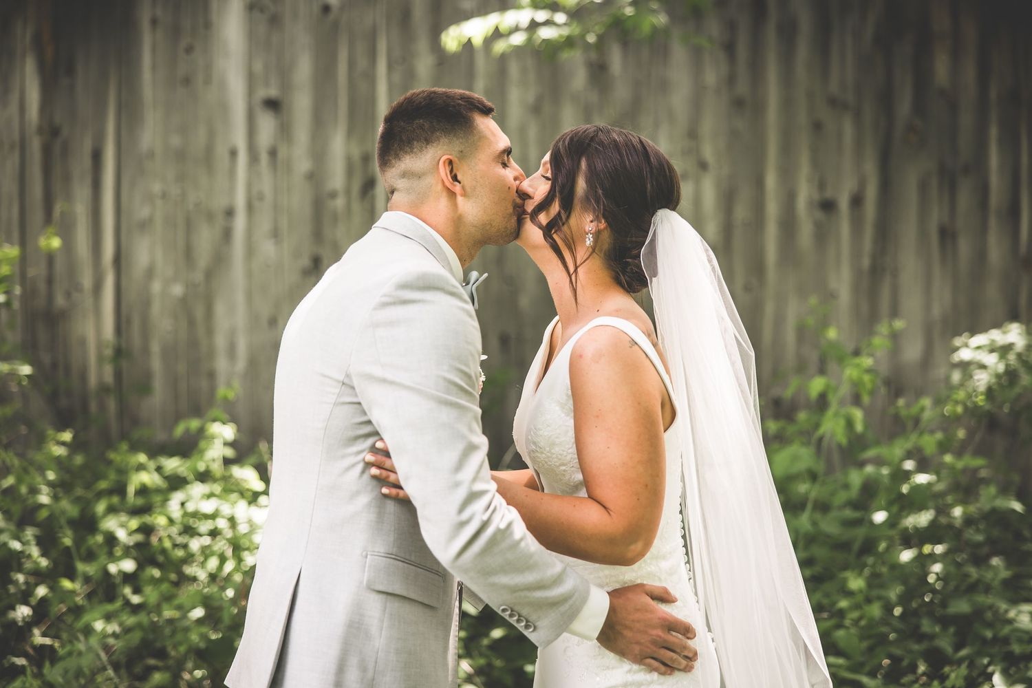 Romantic wedding moment captured against weathered barn backdrop.