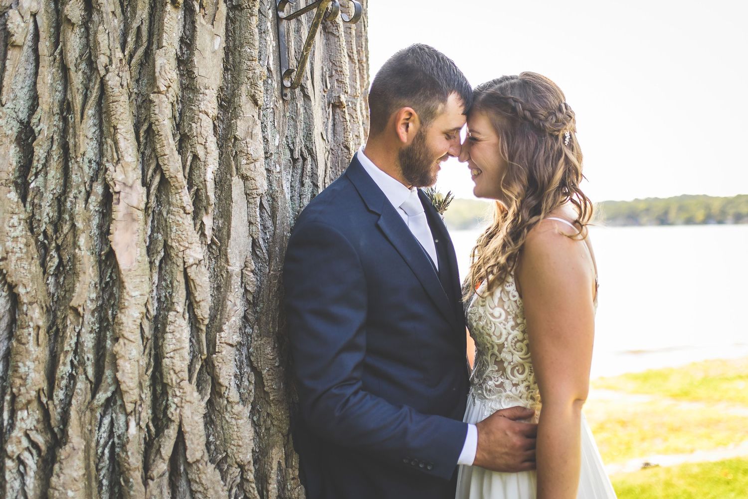 Intimate wedding portrait against a textured tree trunk by the water.