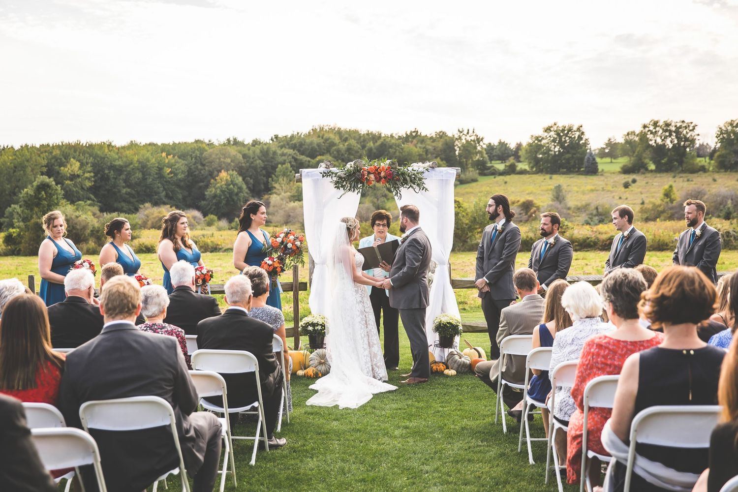 Panoramic view of outdoor wedding ceremony with white chairs and floral arch decorations.