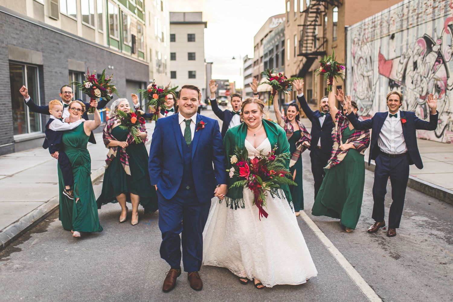 Large wedding party poses together on city street with industrial backdrop.