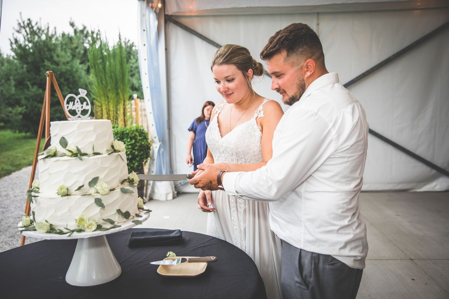 A couple cuts their elegant white wedding cake decorated with greenery at their reception.
