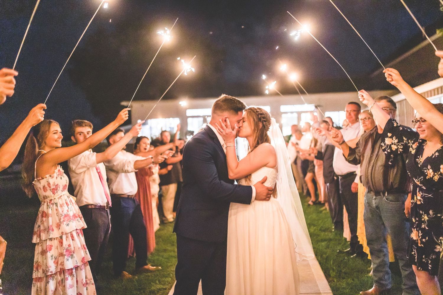 Wedding guests hold sparklers creating a magical nighttime tunnel of lights.