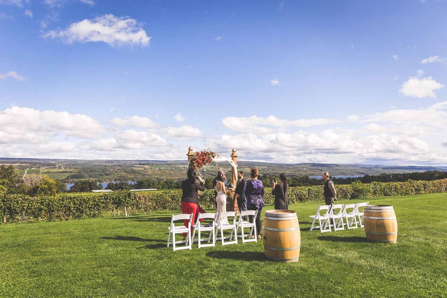 Panoramic view of a hilltop wedding venue with white chairs and wine barrels.