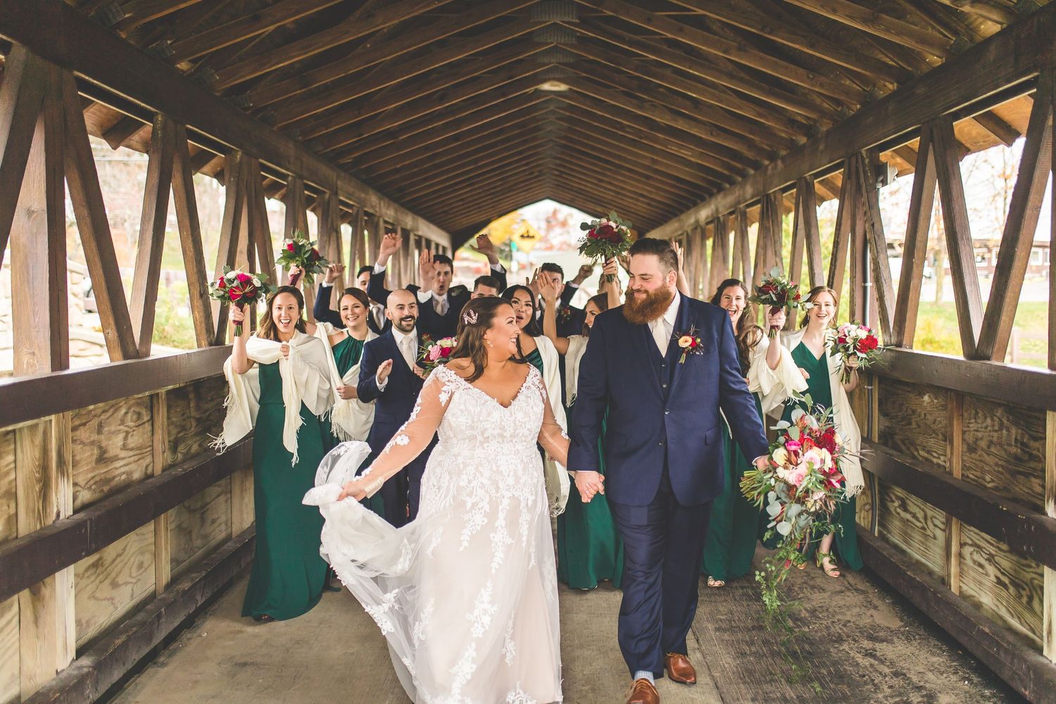 Wedding party lines up inside historic wooden covered bridge for group photos.