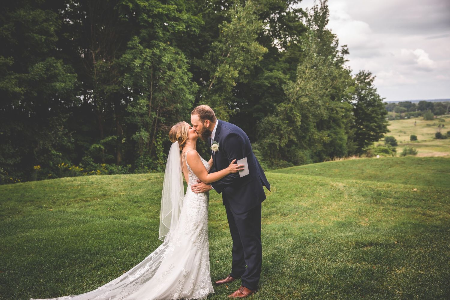 Newlyweds share emotional reactions during outdoor first look with rolling hills in background.