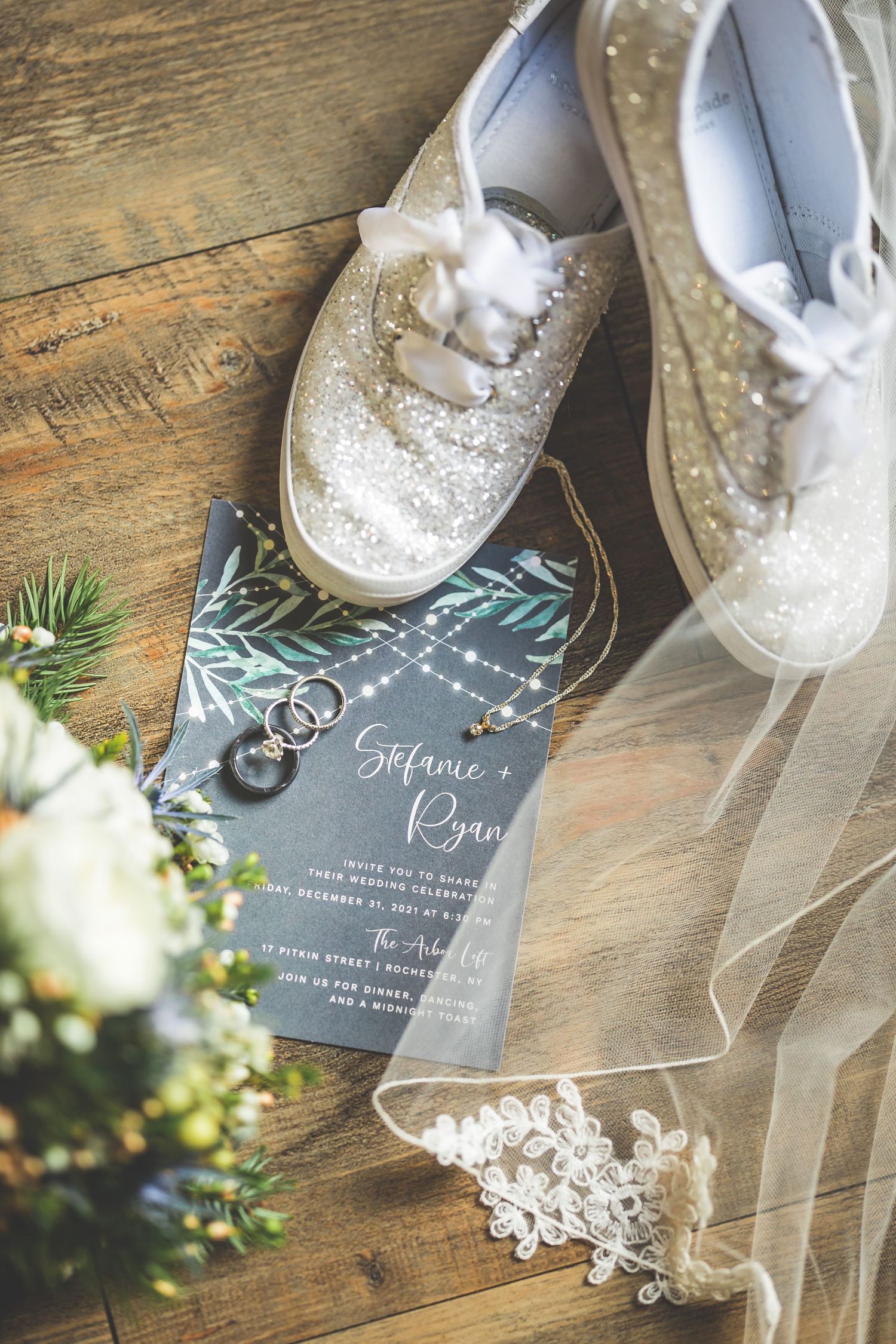 Wedding details with white shoes, veil, and invitation on rustic wooden surface.