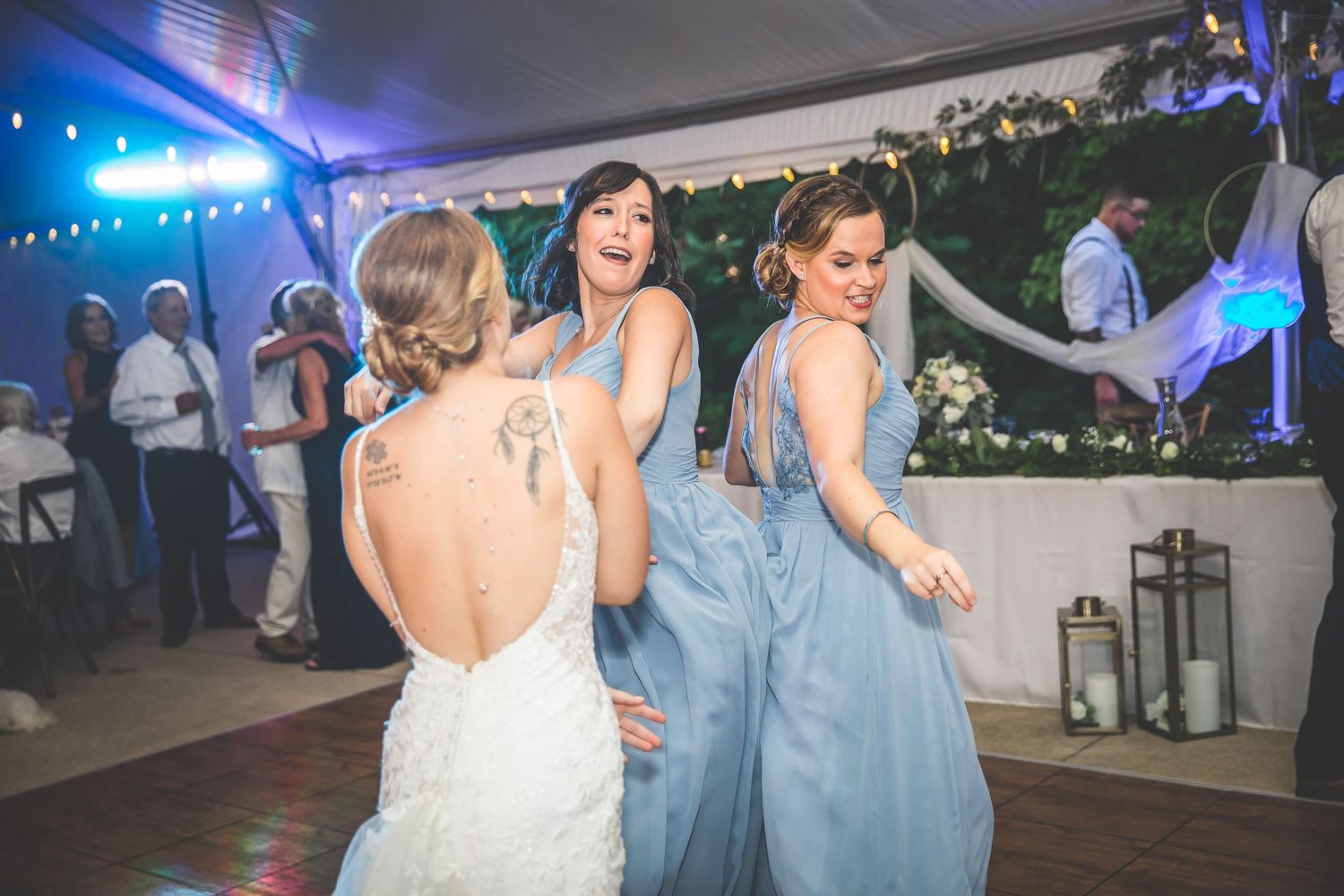 Wedding guests dancing in formal attire under blue lighting at an evening reception.
