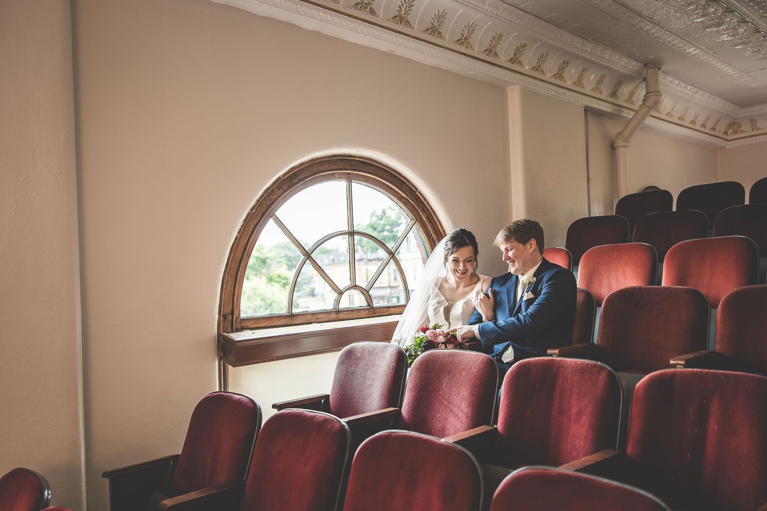 Interior view of ornate venue with red theater seats and arched windows.