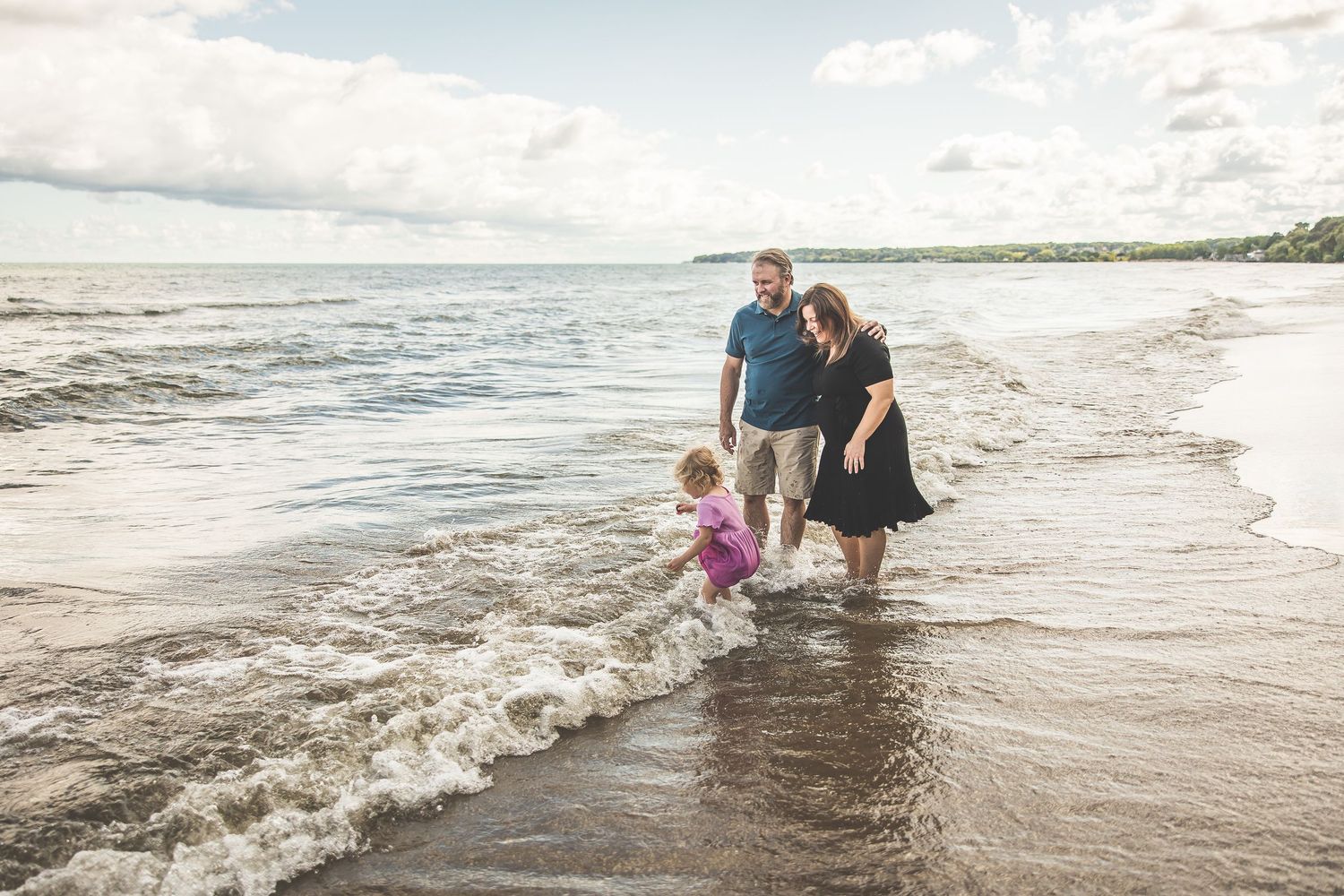 A family plays in ocean waves at the beach during sunset.