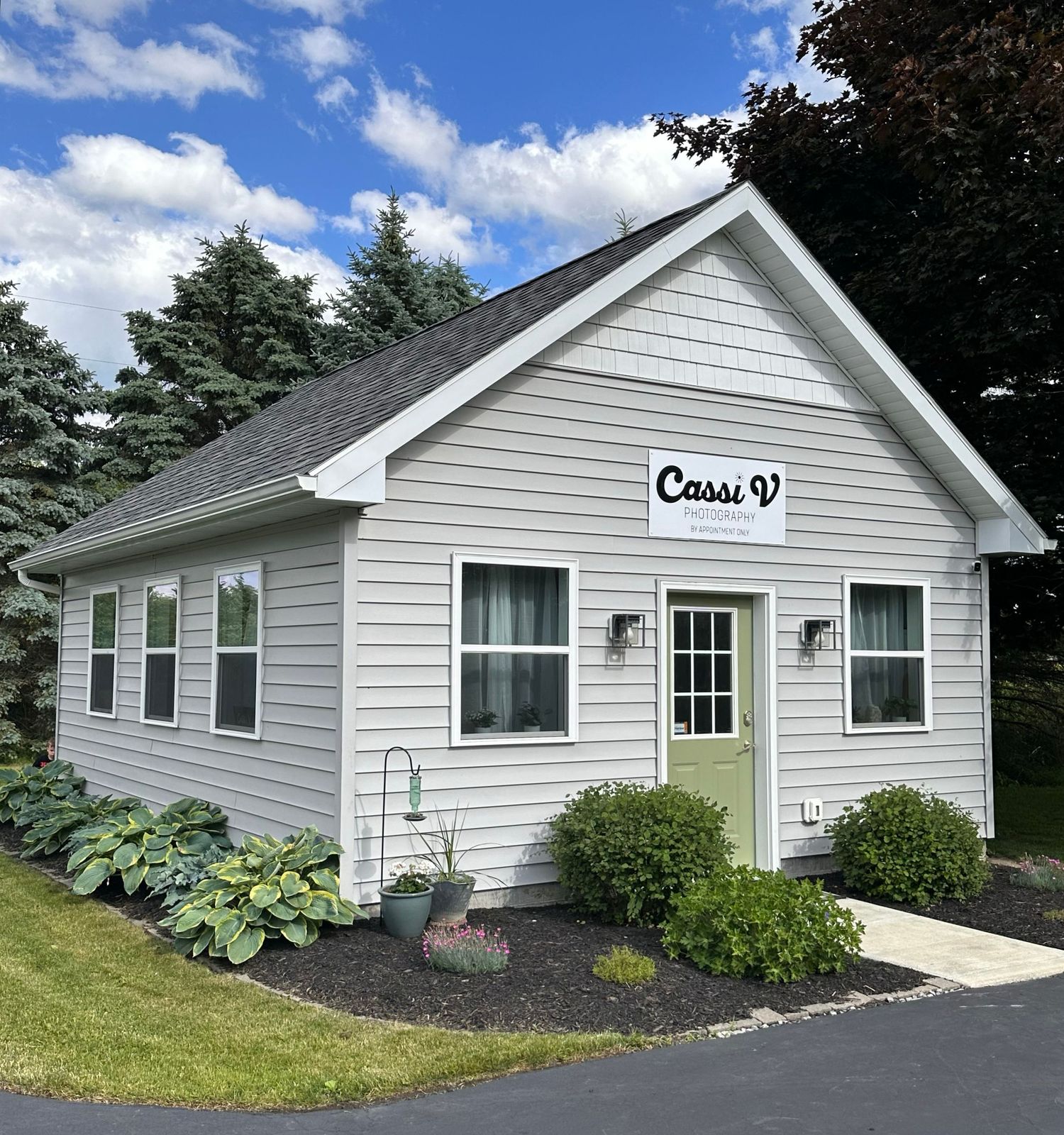 A ranch-style studio with grey siding, landscaping, and multiple windows.