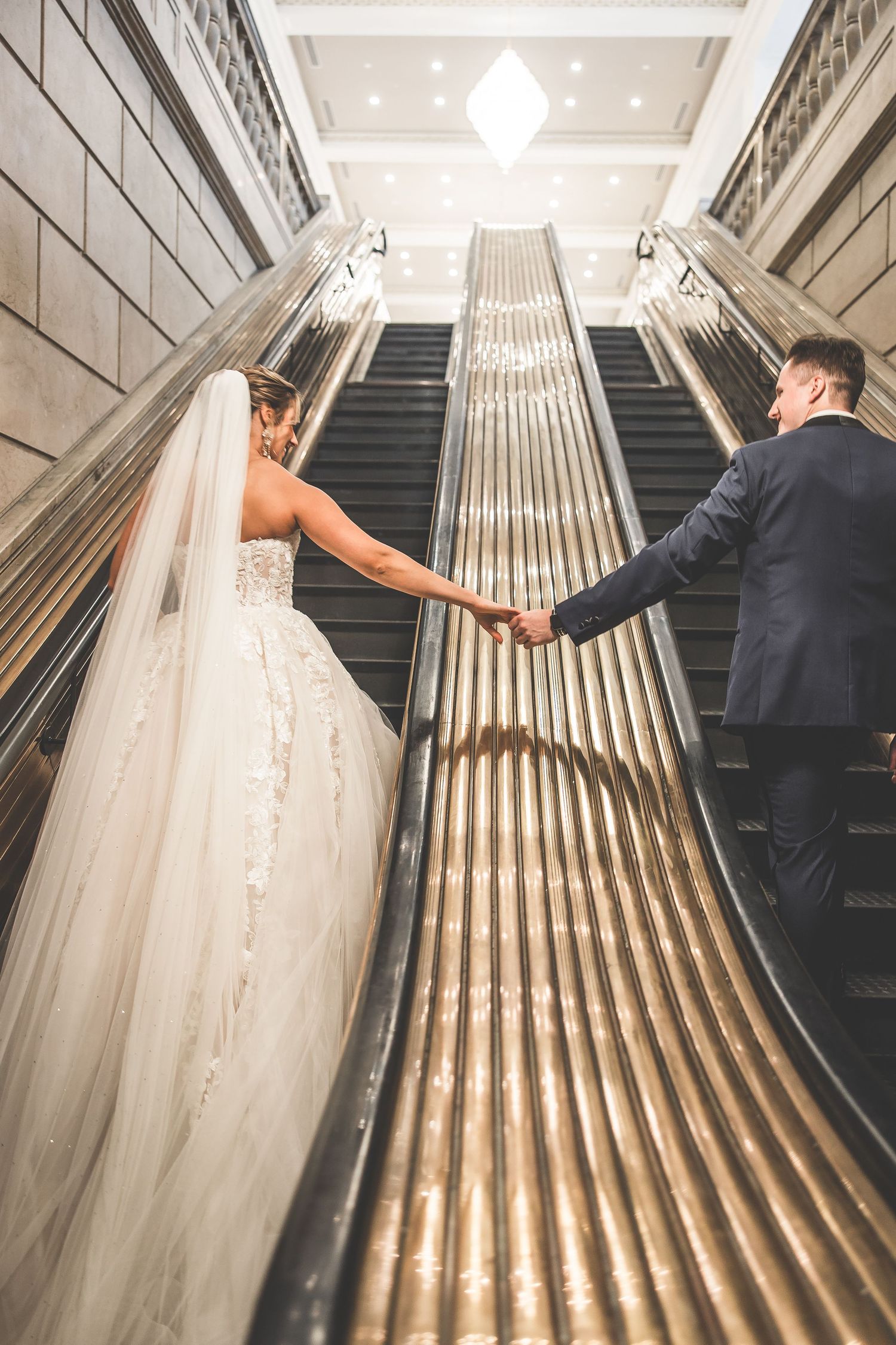 Wedding couple walking down art deco staircase with flowing white dress train.