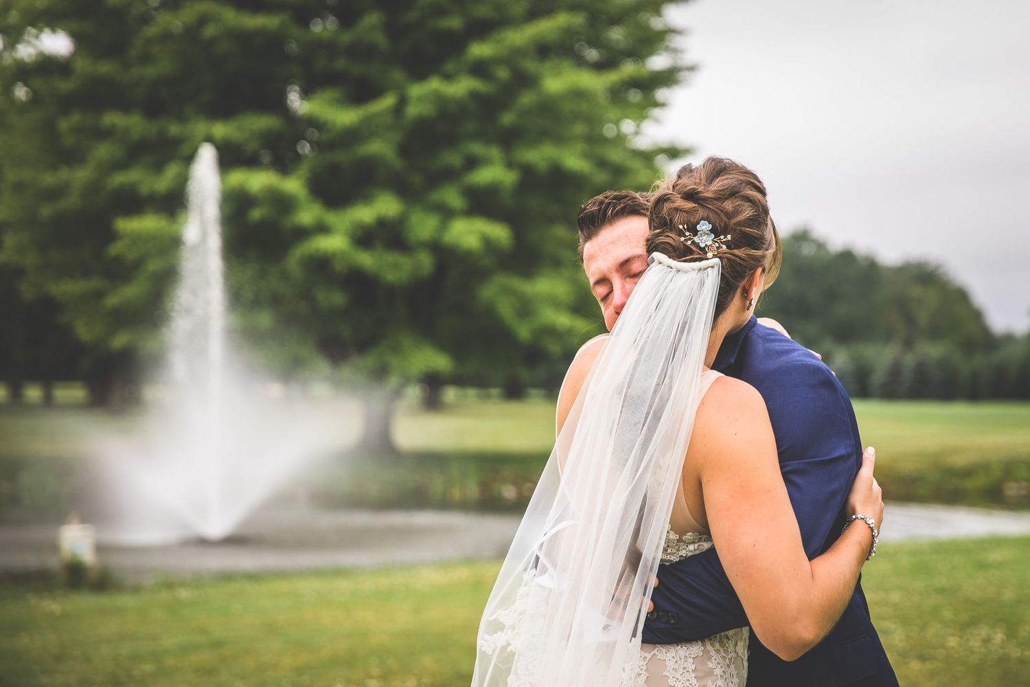 A romantic embrace captured with a fountain in the background during an outdoor wedding.