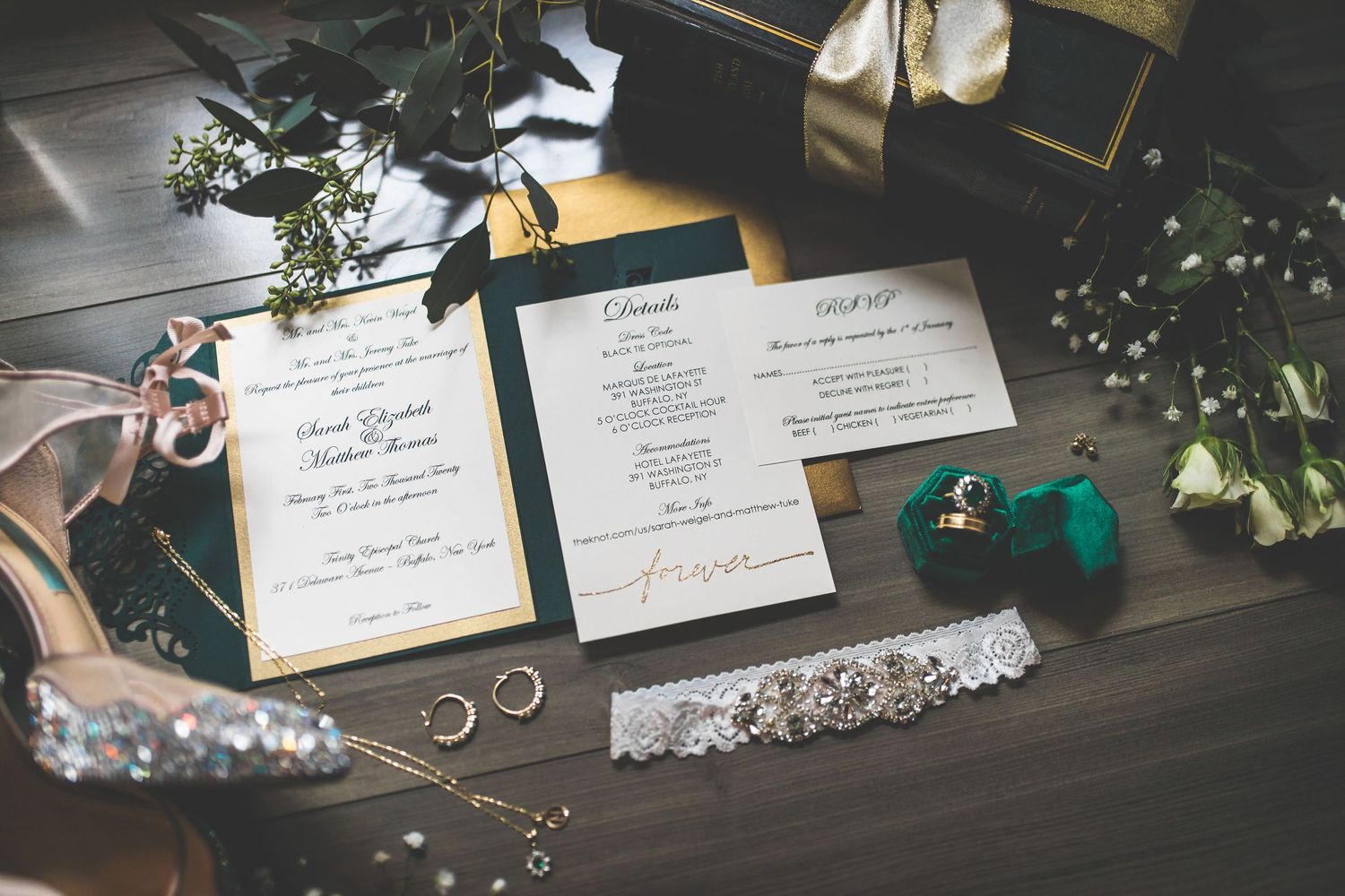 Wedding invitations and rings displayed on a dark wooden surface with decorative elements.