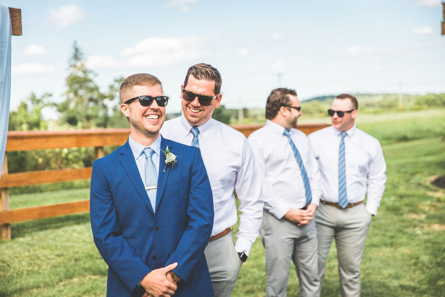 Groomsmen in navy suits and sunglasses pose casually outdoors on a sunny day.