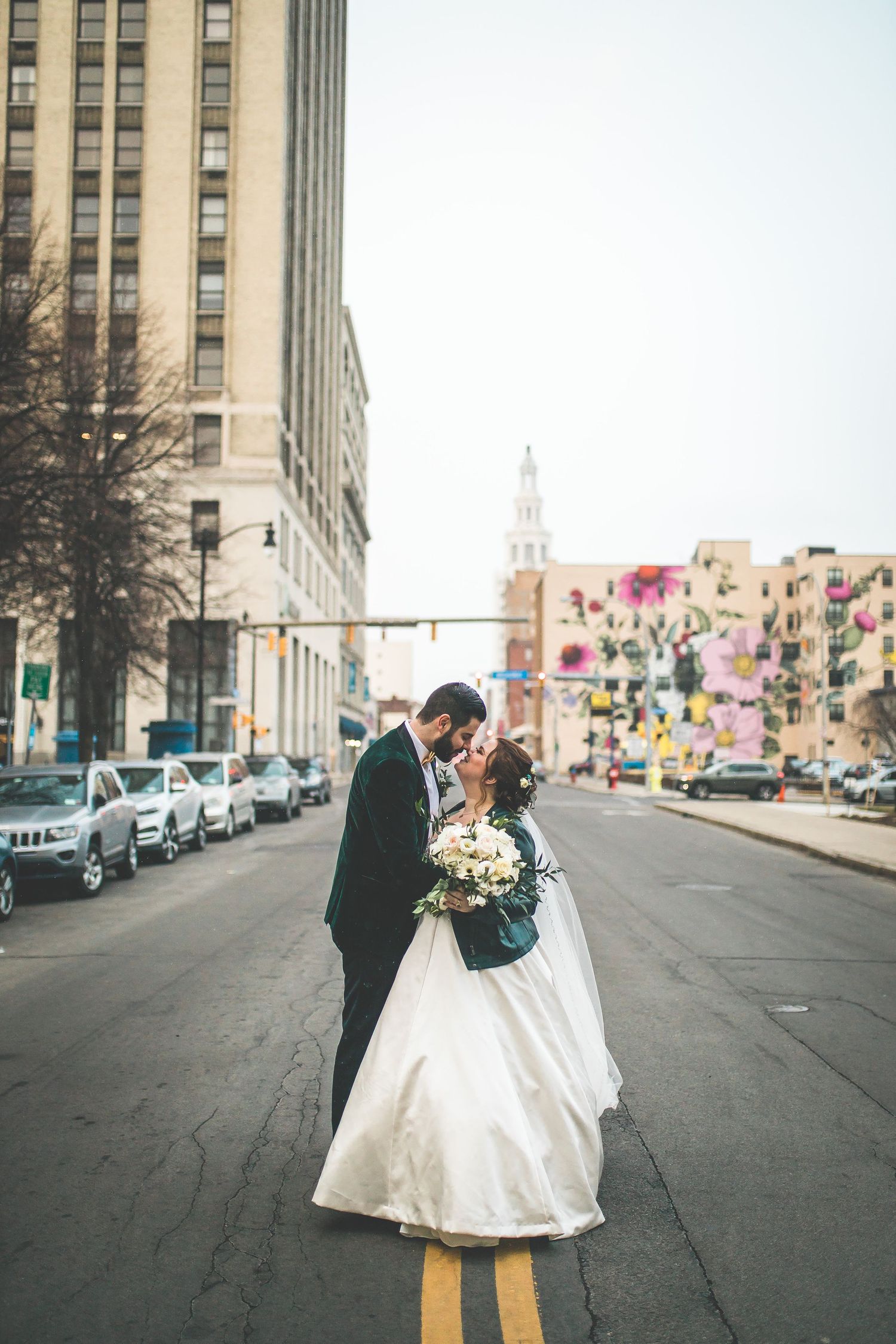 Wedding couple embracing in the middle of a city street with tall buildings and colorful murals.