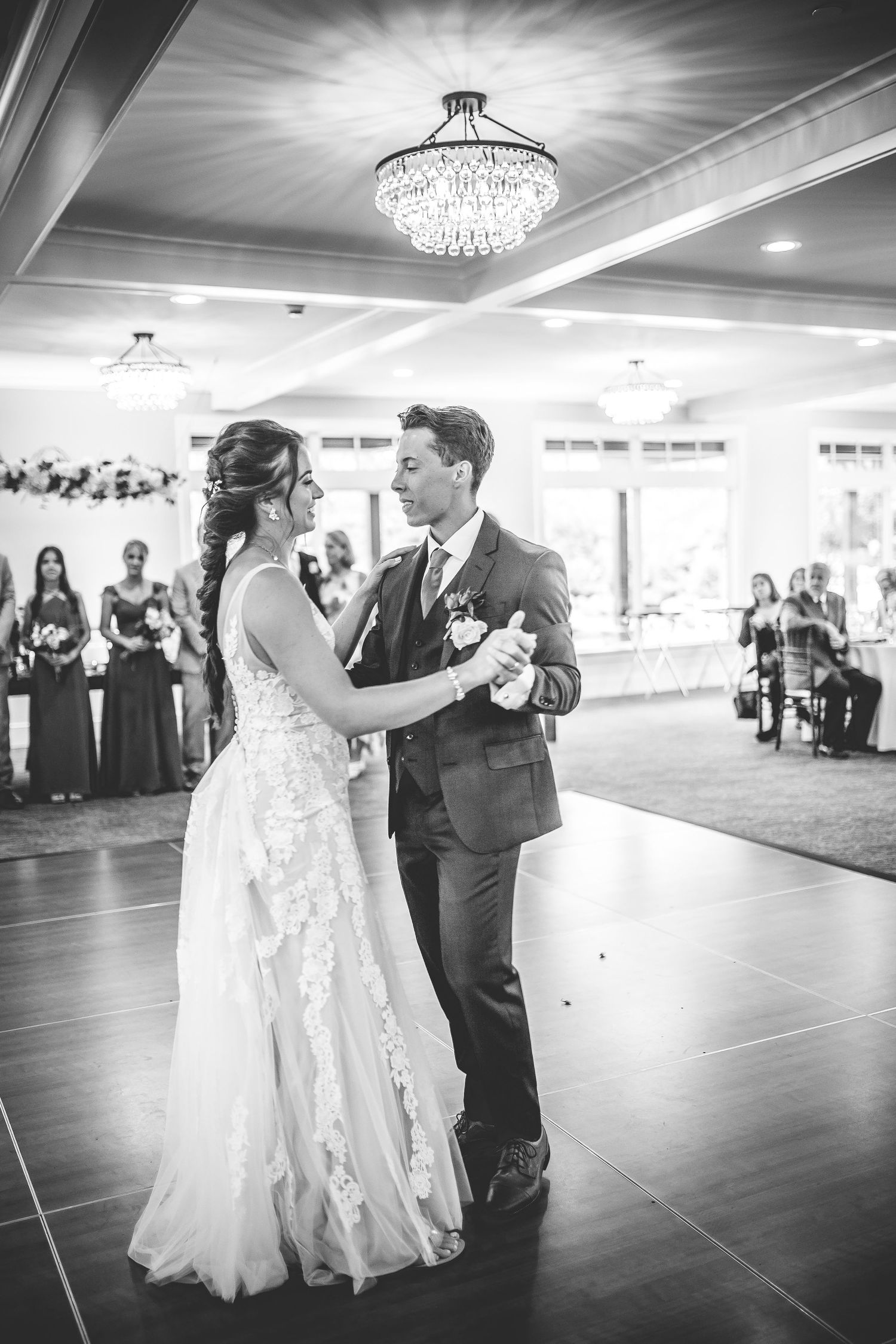 Black and white photos of a couple's first dance at their wedding reception under elegant chandeliers.