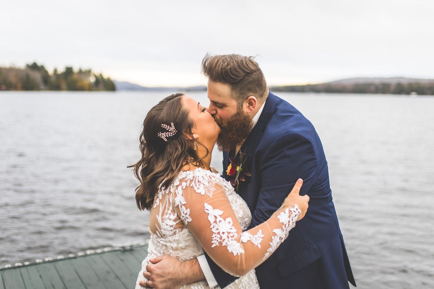 A couple shares an intimate moment on a wooden dock overlooking a serene lake.