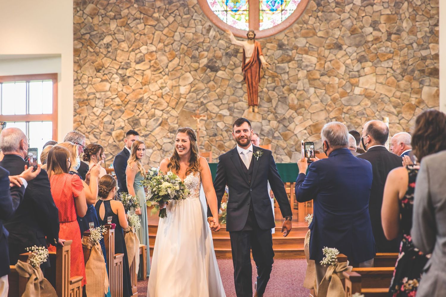 Wedding ceremony in a rustic stone church with stained glass windows and wooden pews.