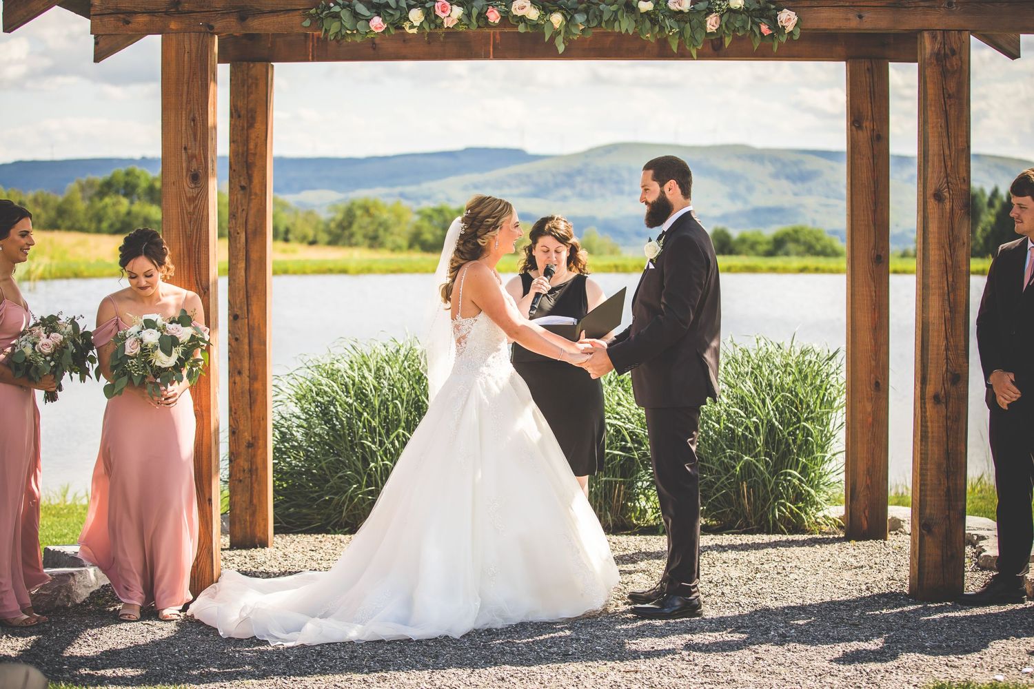 A wedding ceremony under a wooden pergola with lake and mountain views in the background.
