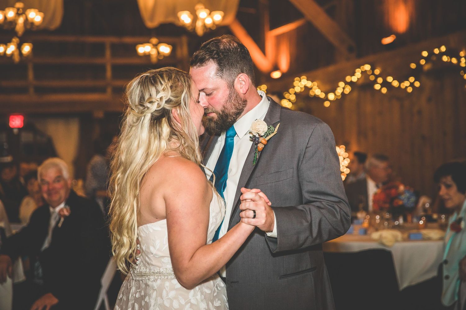 Couple shares their first dance at rustic barn wedding reception with string lights.