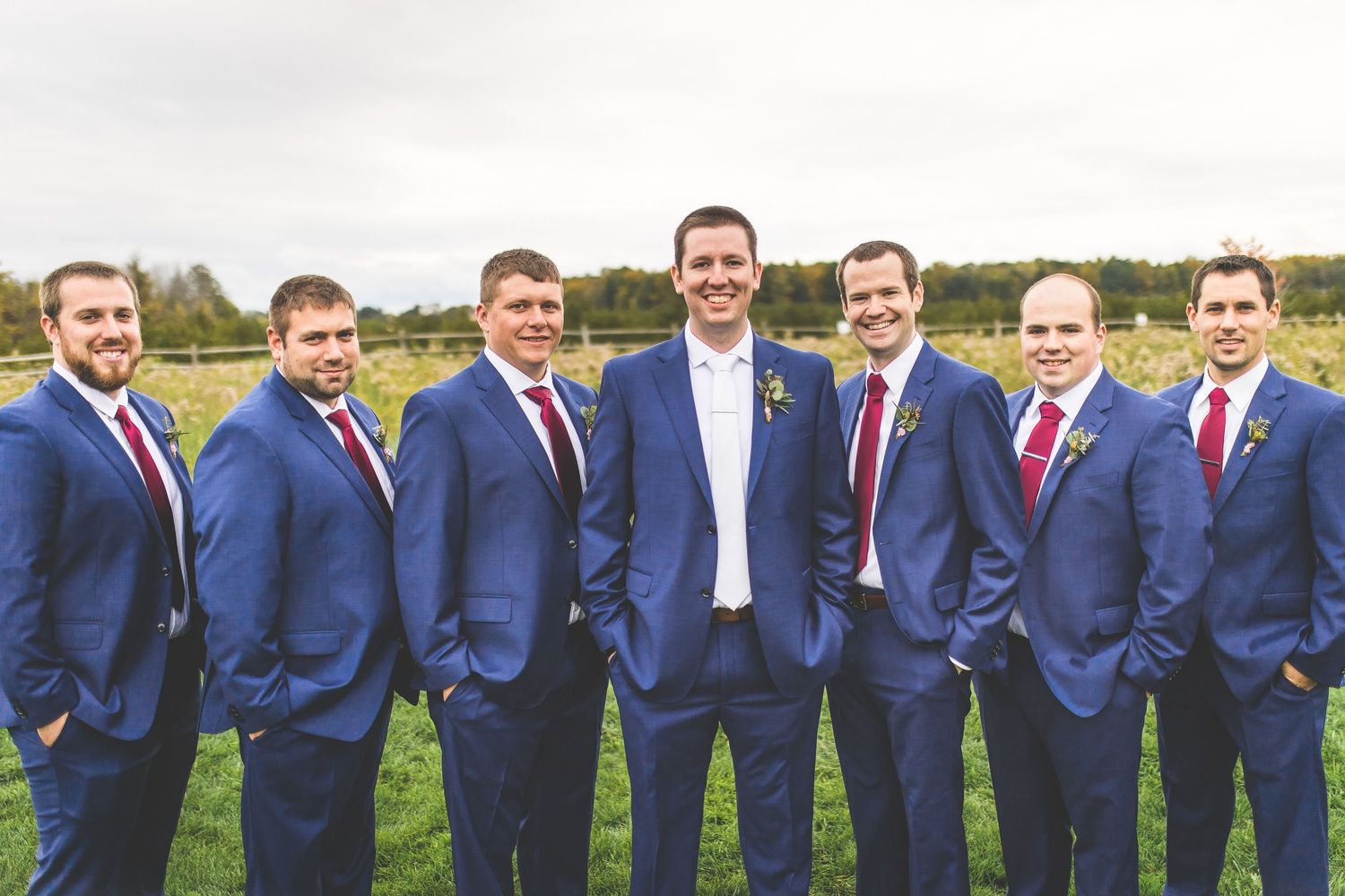 Groomsmen in navy blue suits pose together outdoors for wedding party photos.