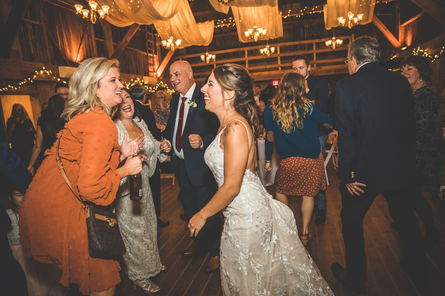 Lively dance floor moments during wedding reception in rustic barn setting with warm lighting.