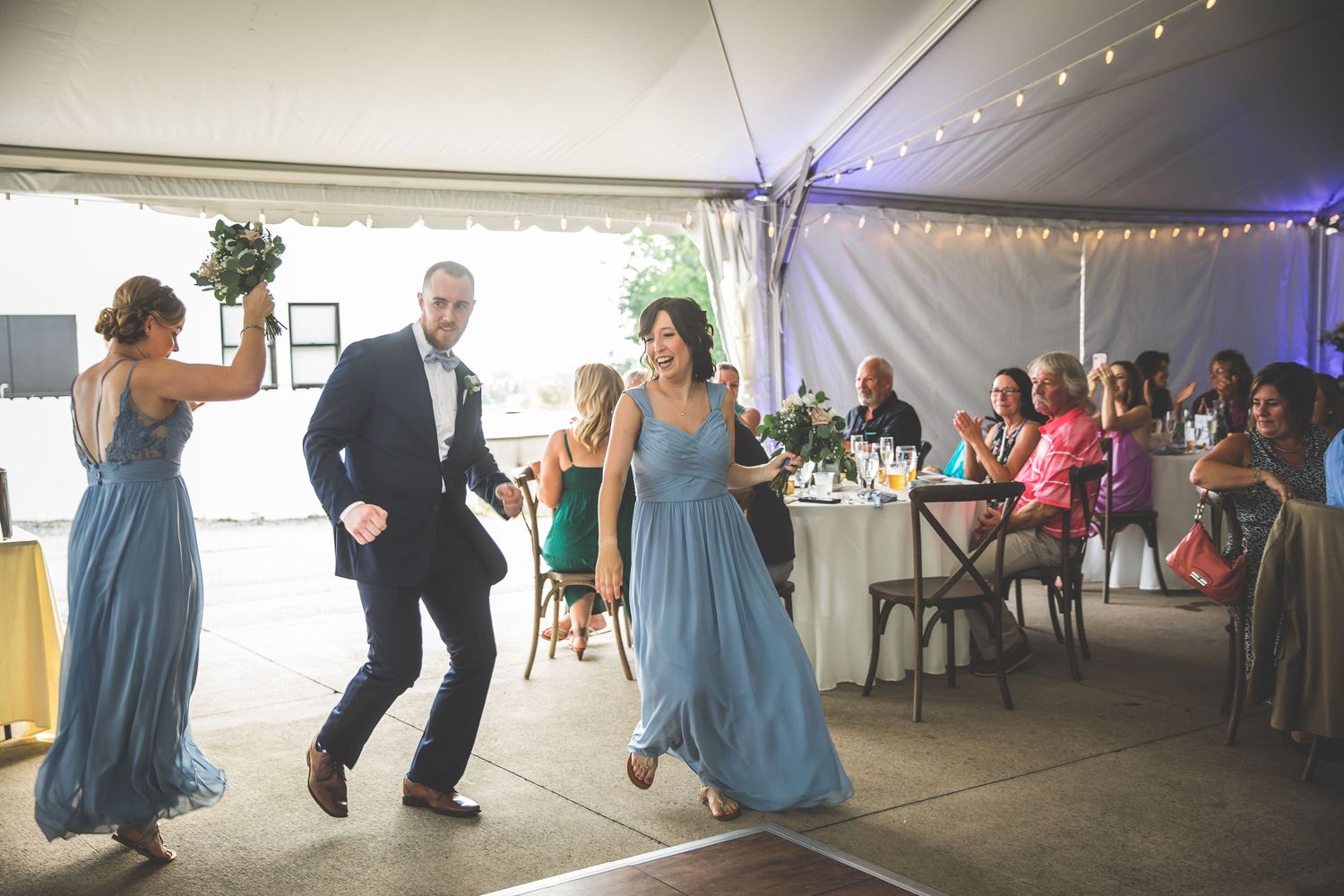 Wedding reception dance party under a white tent with string lights and guests dancing.