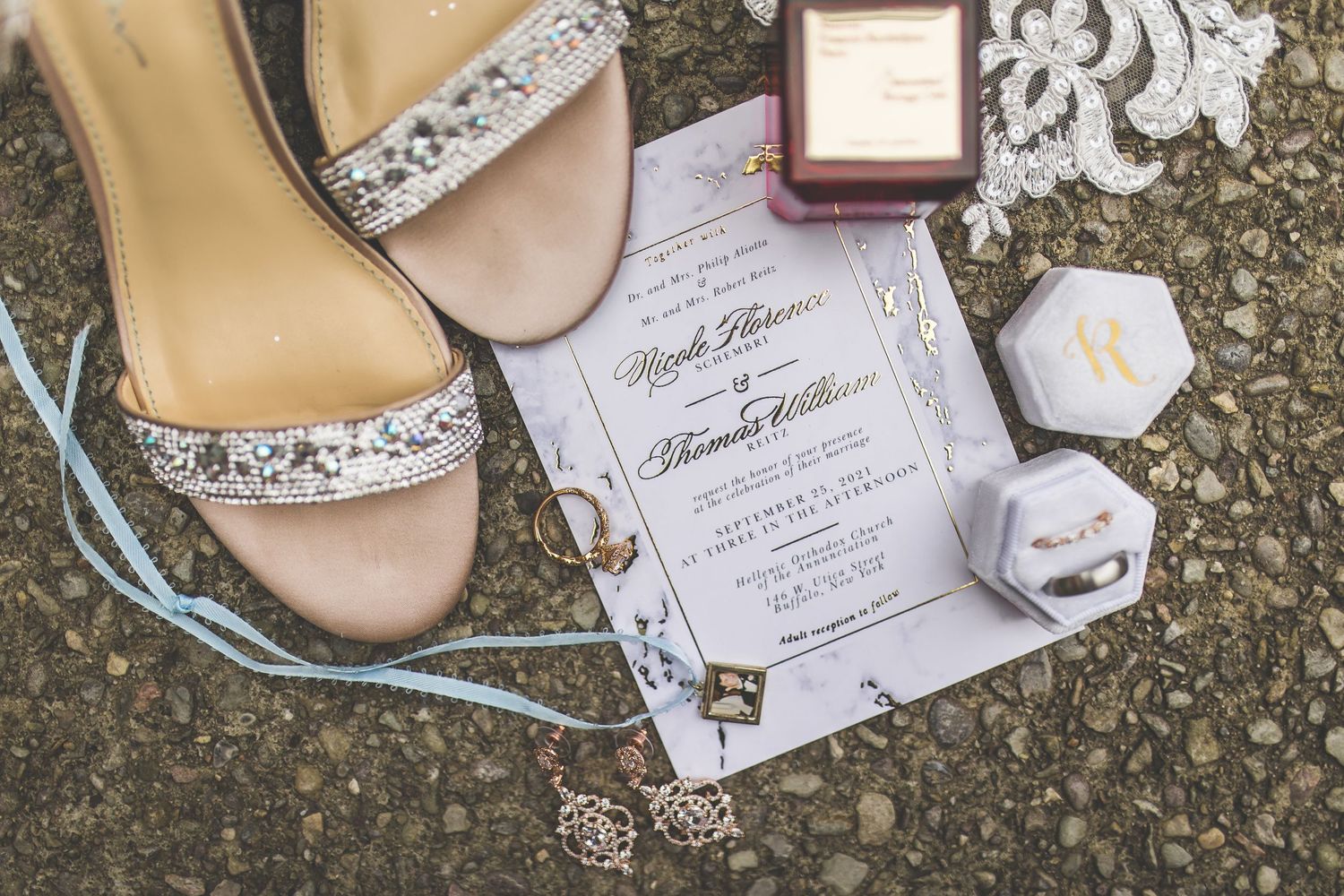 Wedding details flatlay with invitation, rings, and elegant bridal shoes on textured surface.